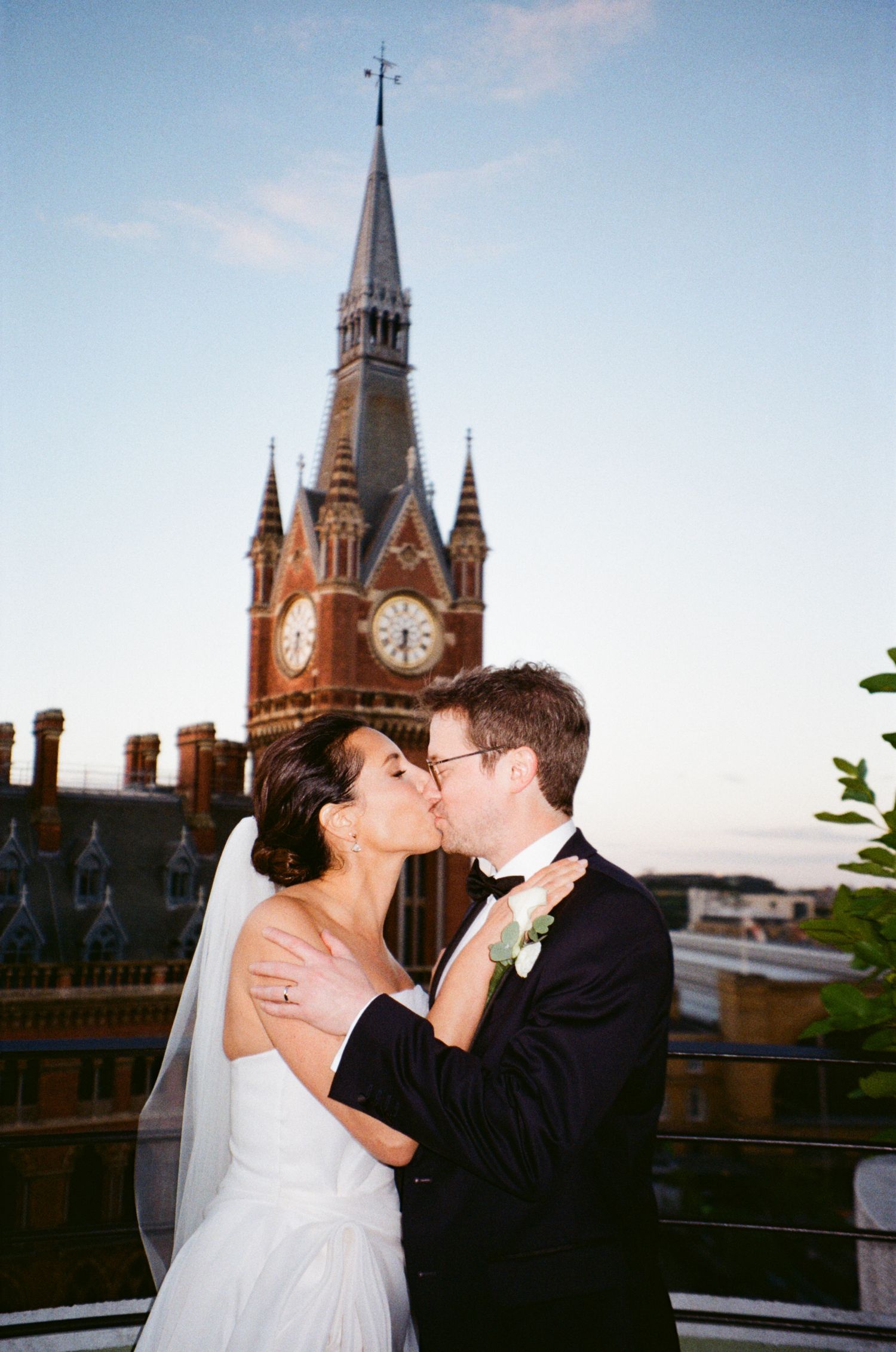 A couple shares a romantic kiss on a rooftop terrace with the historic St. Pancras Renaissance Hotel's spires in the background.