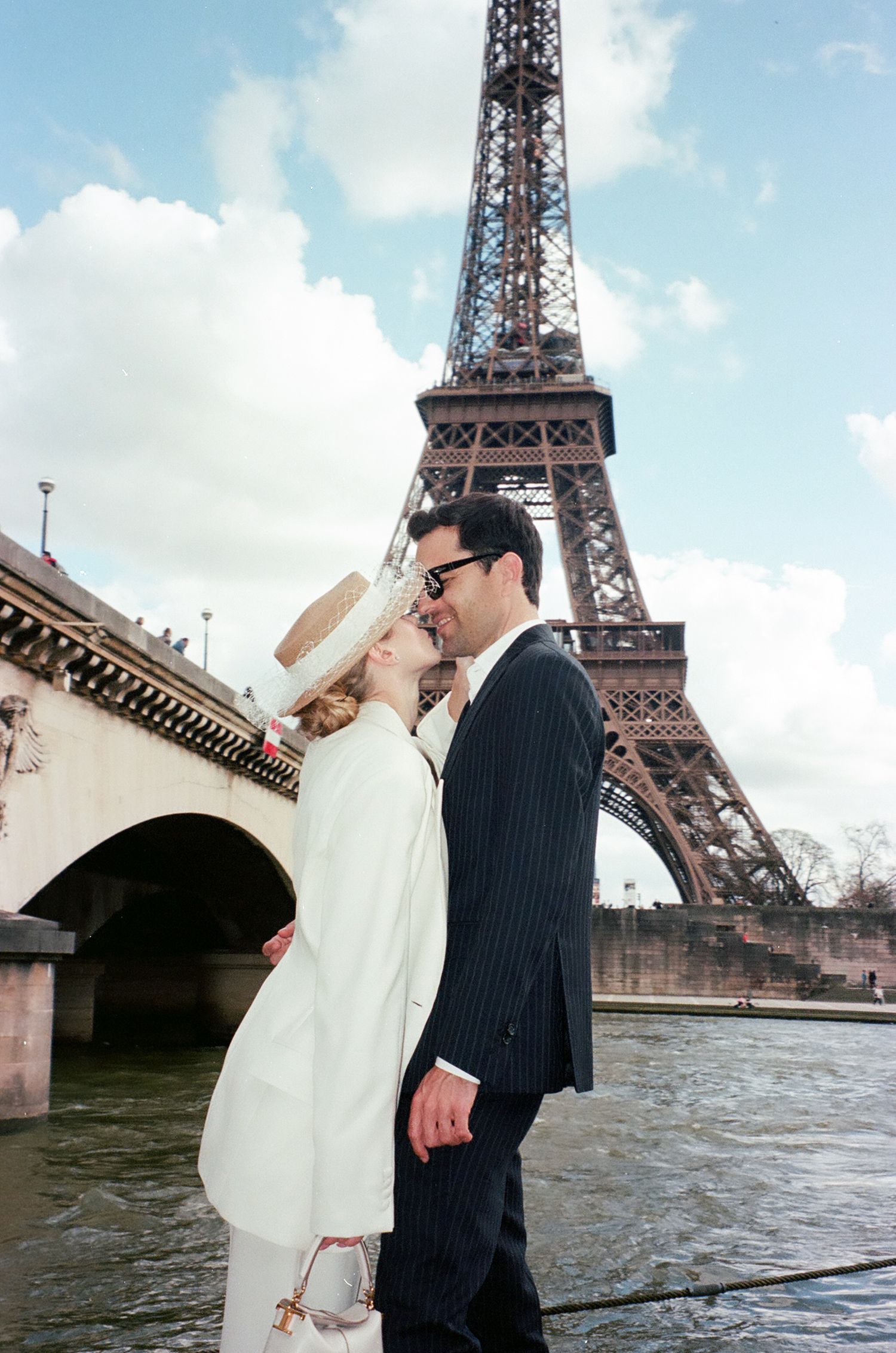A couple shares a romantic kiss in front of the iconic Eiffel Tower in Paris on a cloudy day.