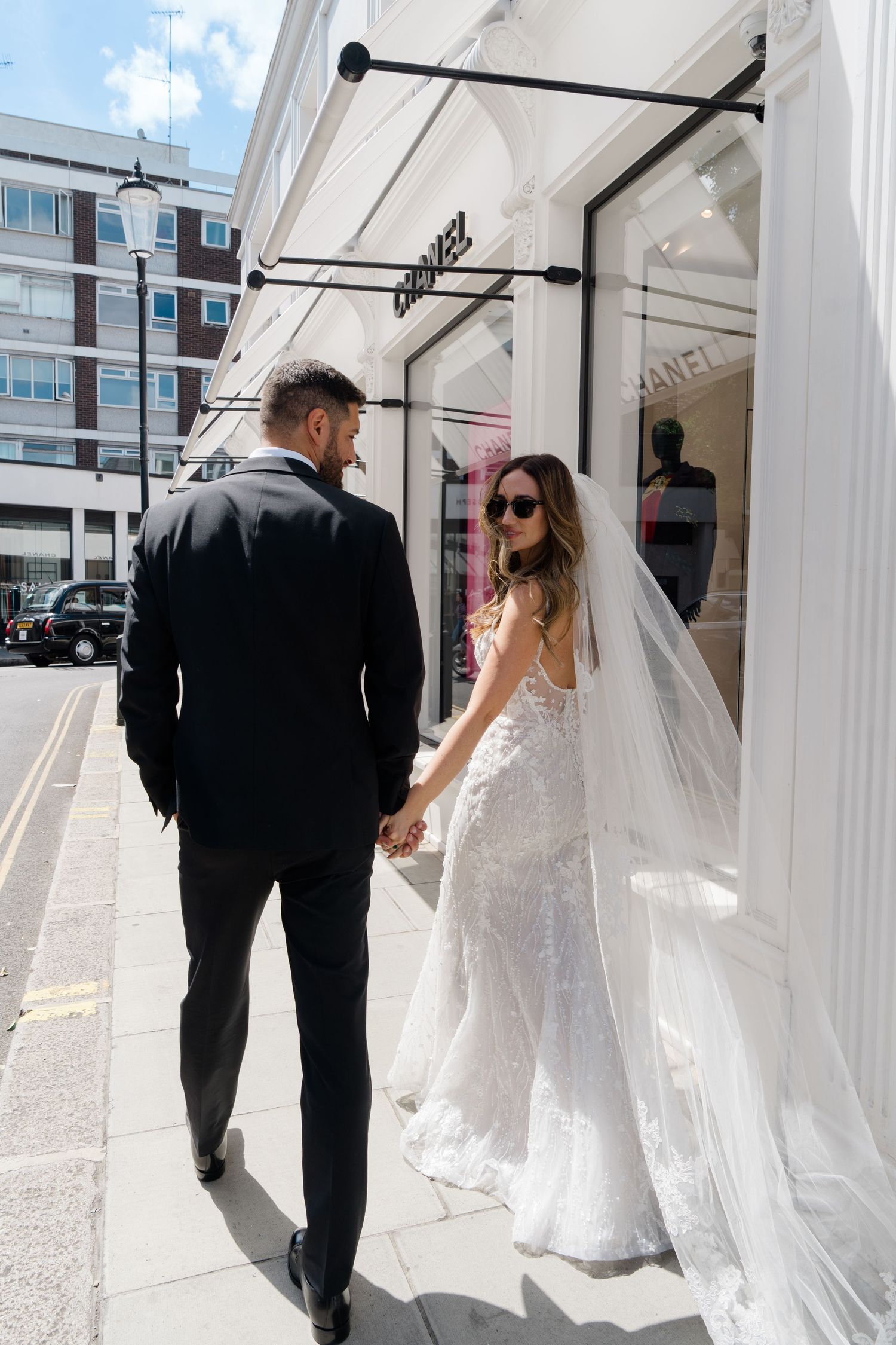 Wedding couple walking through a modern white hallway with large windows.
