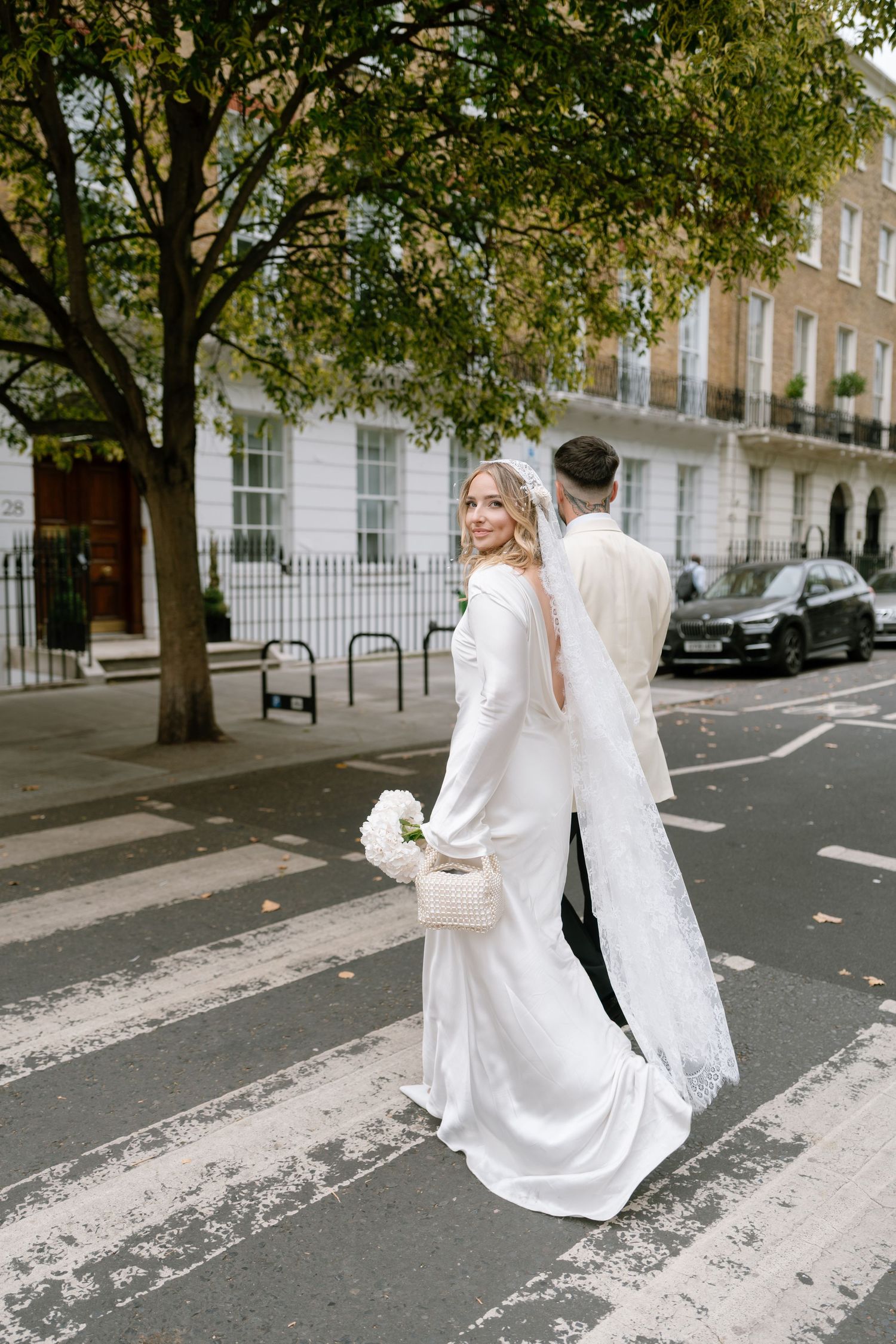 A couple in white attire dances playfully on a London street with classic Georgian buildings in the background.