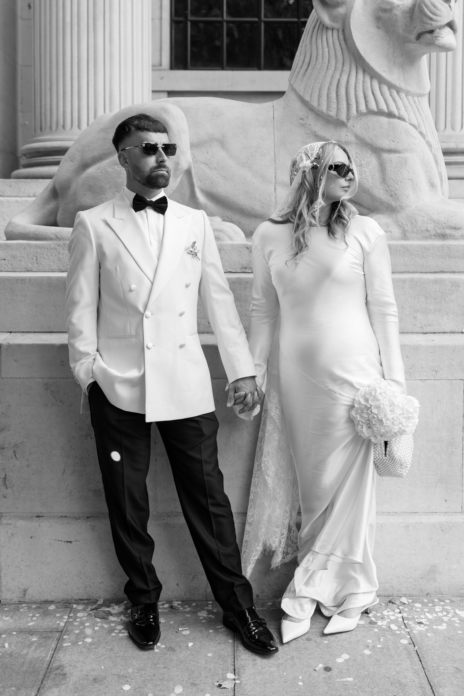 A wedding couple poses against a classical building facade with white columns.