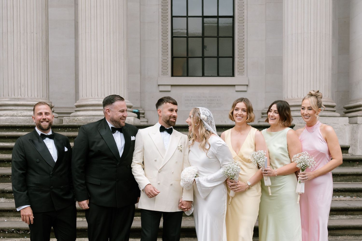 Wedding party lined up against classic stone columns in formal attire.