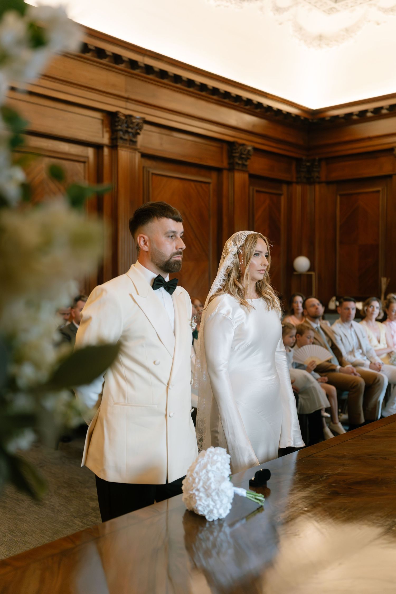 Newlyweds share a dance moment in a grand ballroom with wooden walls and decorative moldings.