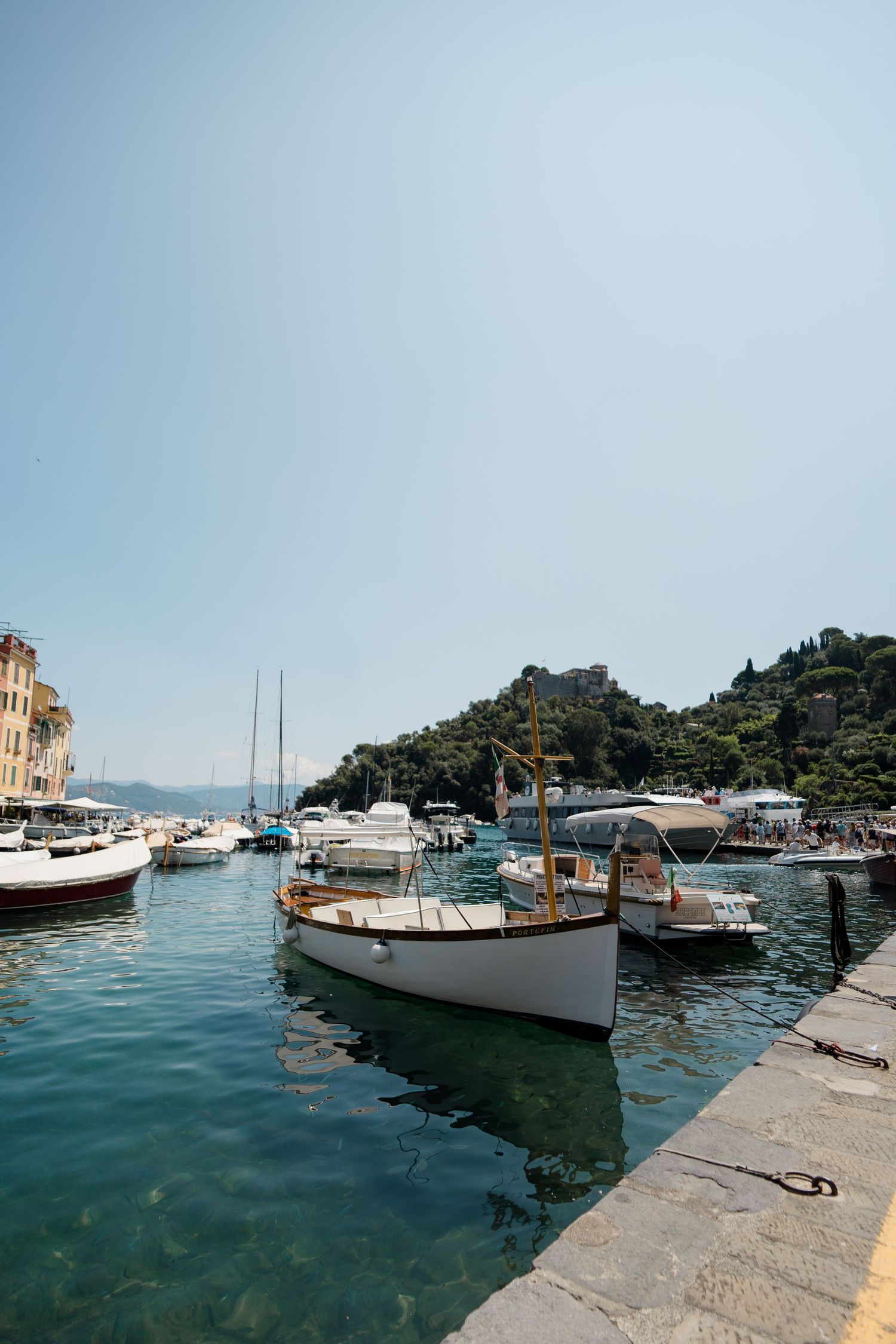 Scenic view of white boats moored in the crystal clear harbor of Portofino, Italy on a sunny day.