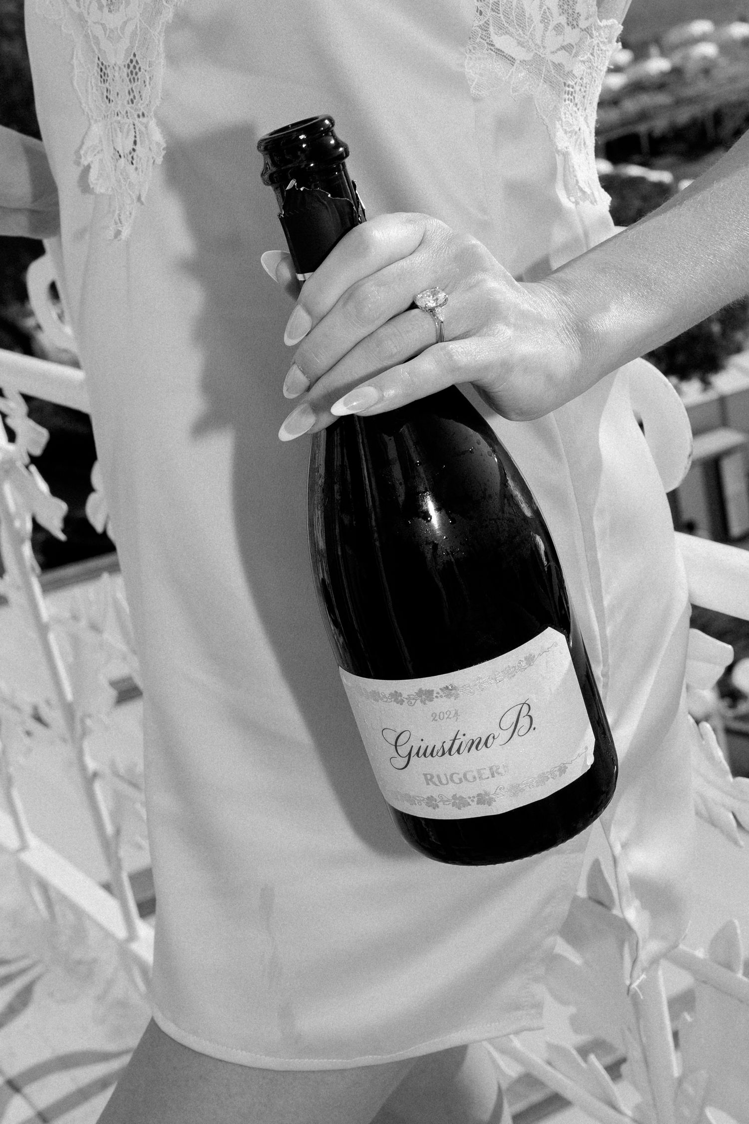 Black and white close-up of a bride in a lace slip dress holding a large bottle of Giustino B. Ruggeri.