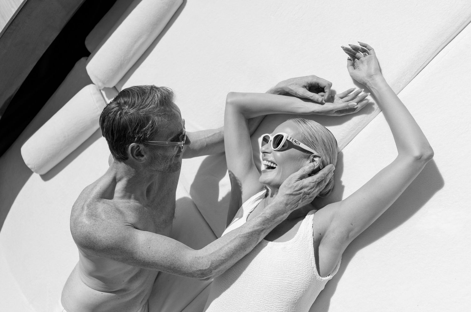 Black and white photo of a couple laughing and posing together in bright sunlight on a boat.