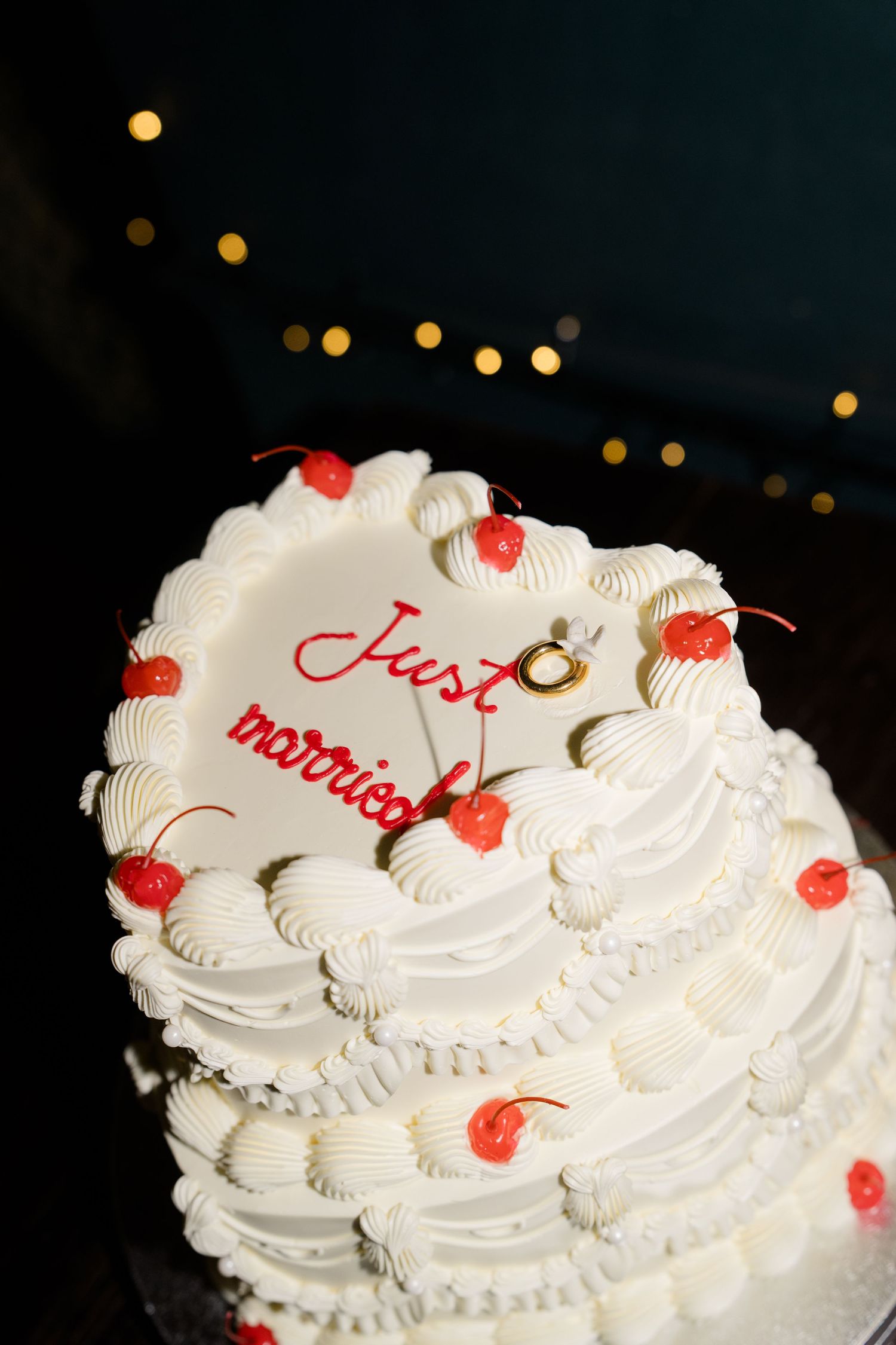 White tiered wedding cake decorated with red cherries and Just Married inscription with gold rings.