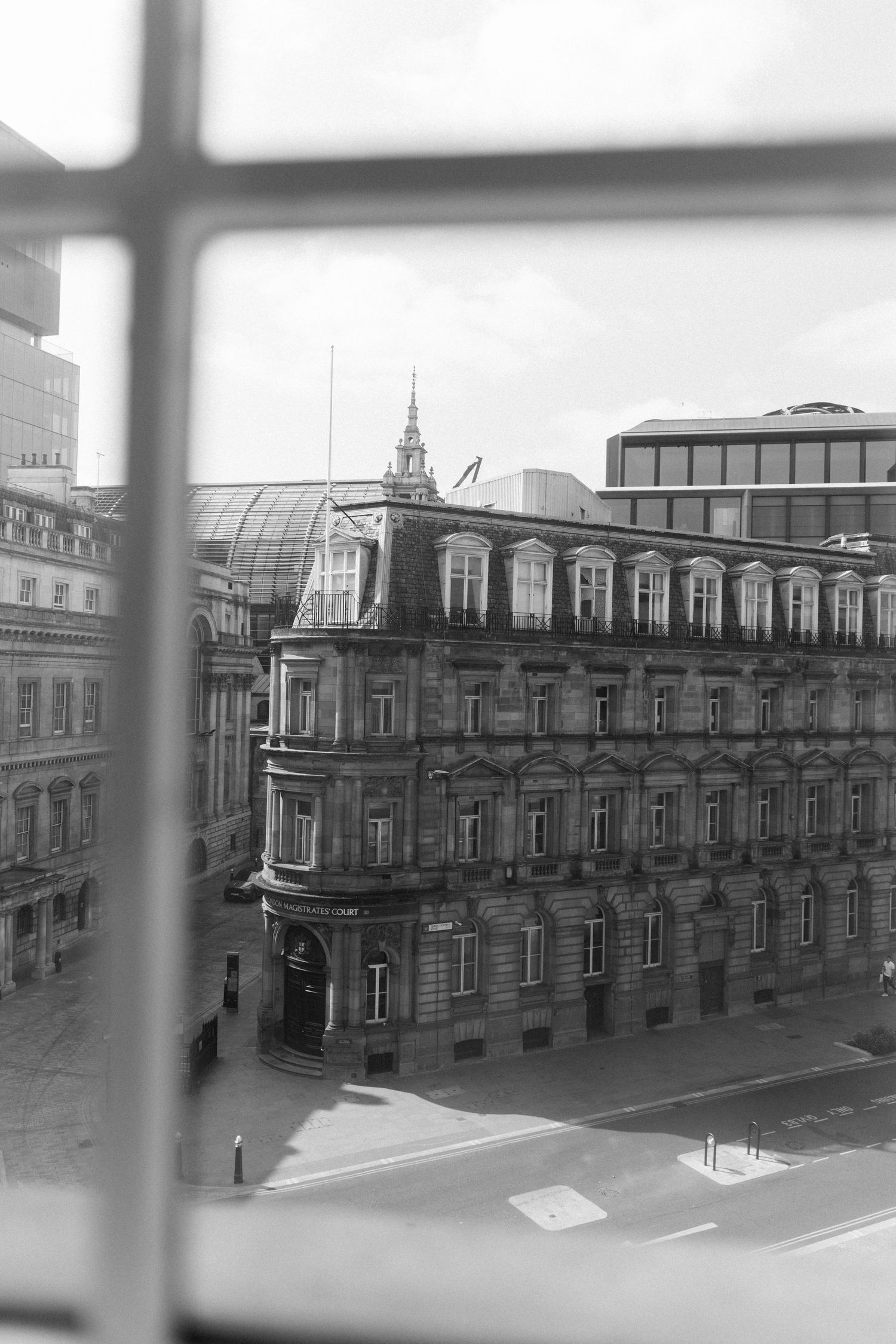 Black and white aerial view of a grand Victorian building facade captured through a window frame in an urban setting.