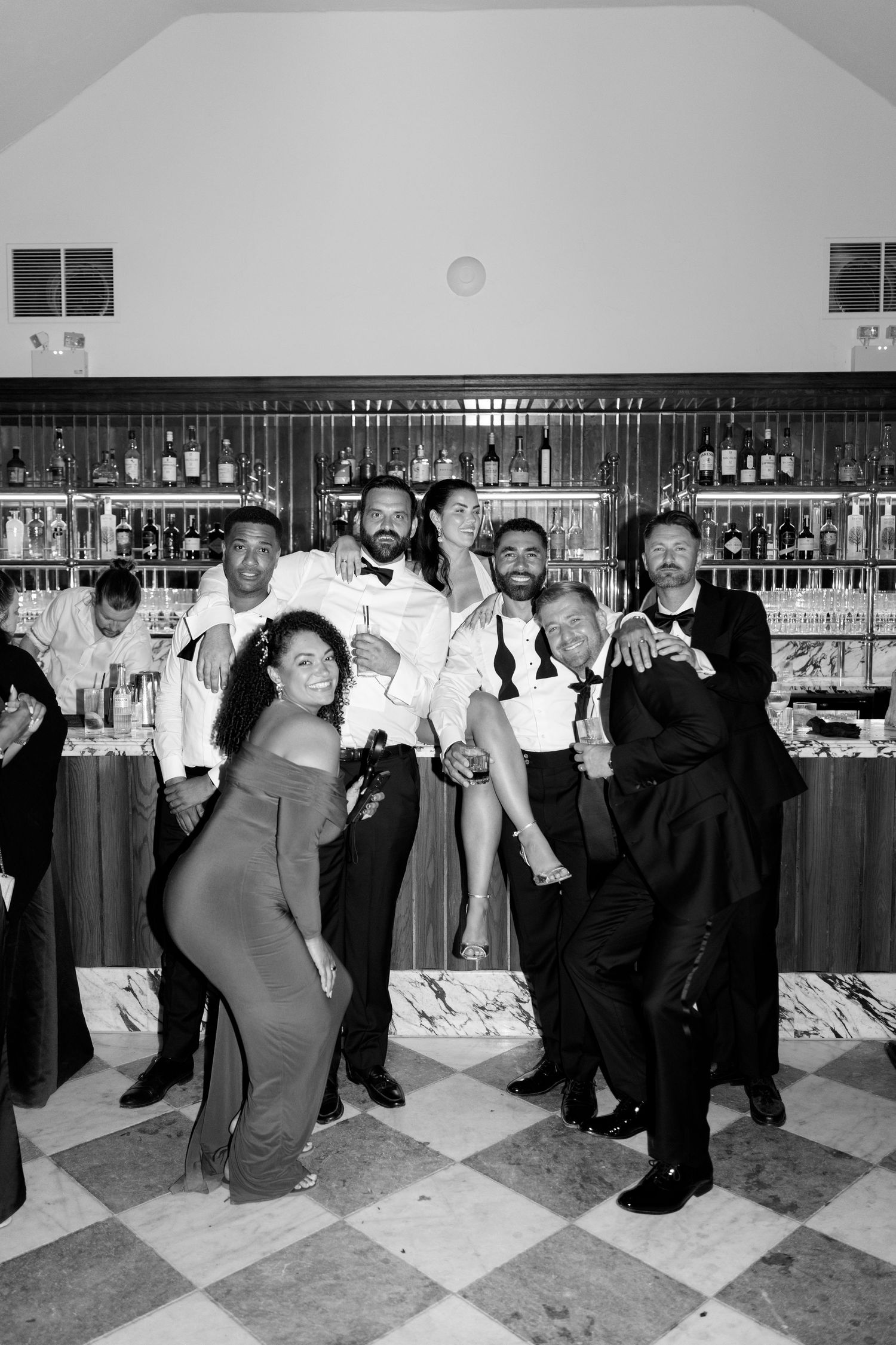 Black and white photo of a lively group posing together in front of a well-stocked wedding bar.
