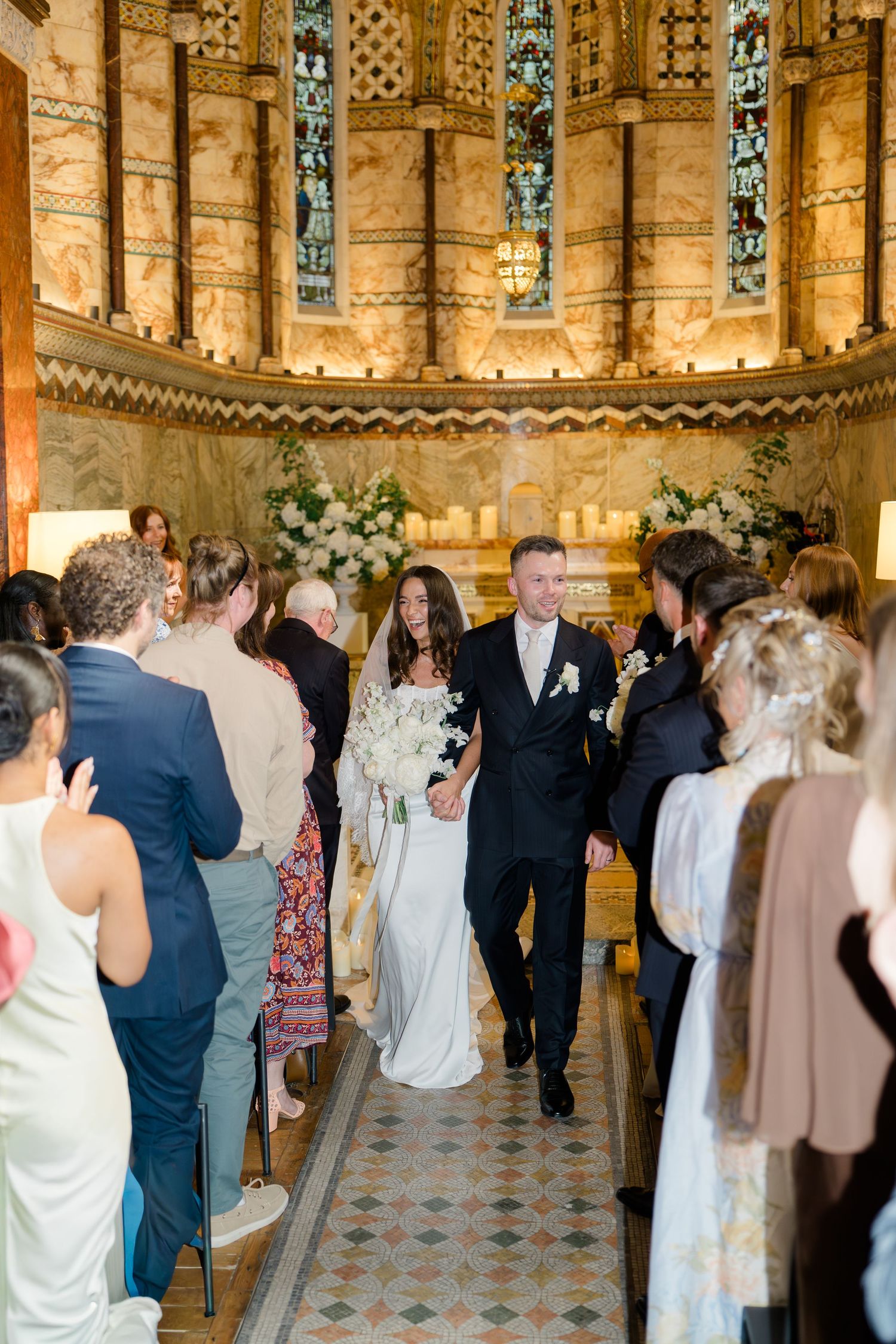 Bride and groom walk hand in hand down the aisle of a stunning ornate chapel after their wedding ceremony.
