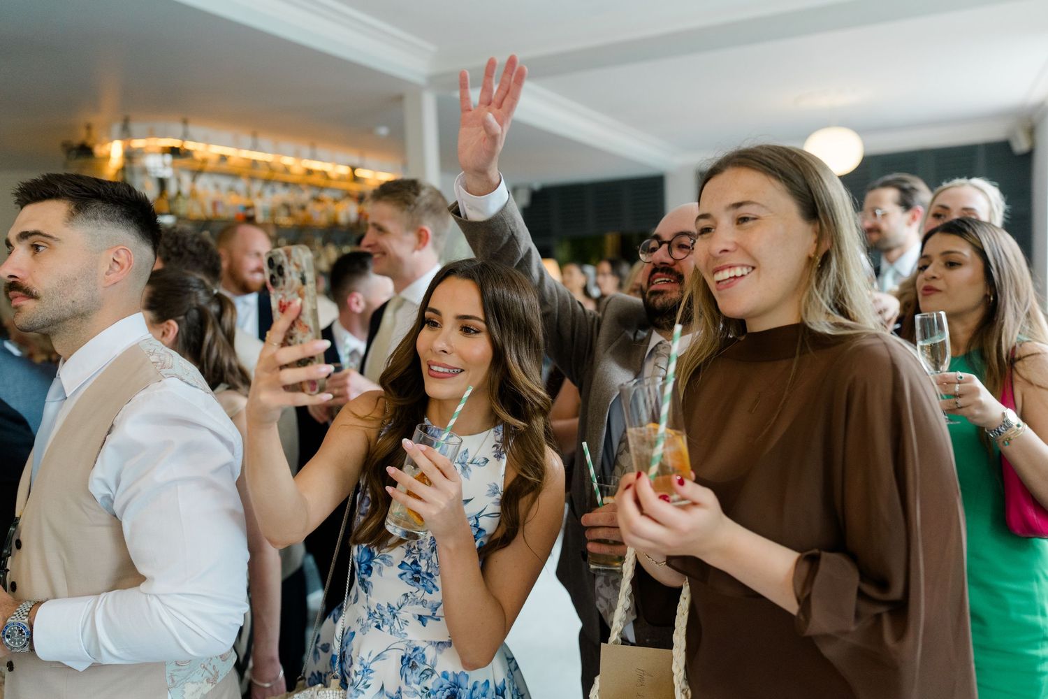 Smiling wedding guests socializing and holding champagne glasses at lively indoor cocktail reception.