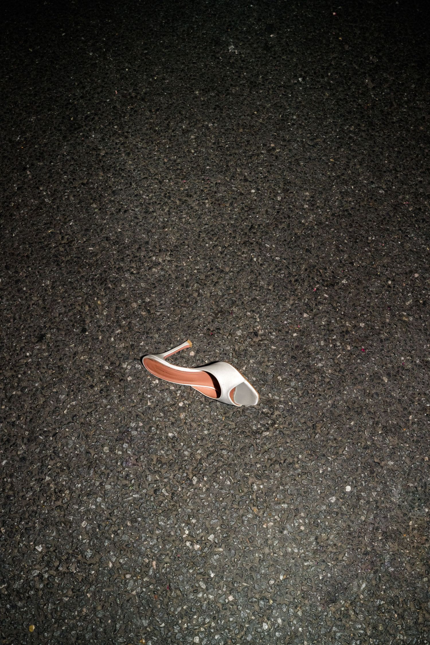 Single white and tan high heel shoe abandoned on dark asphalt pavement at night.