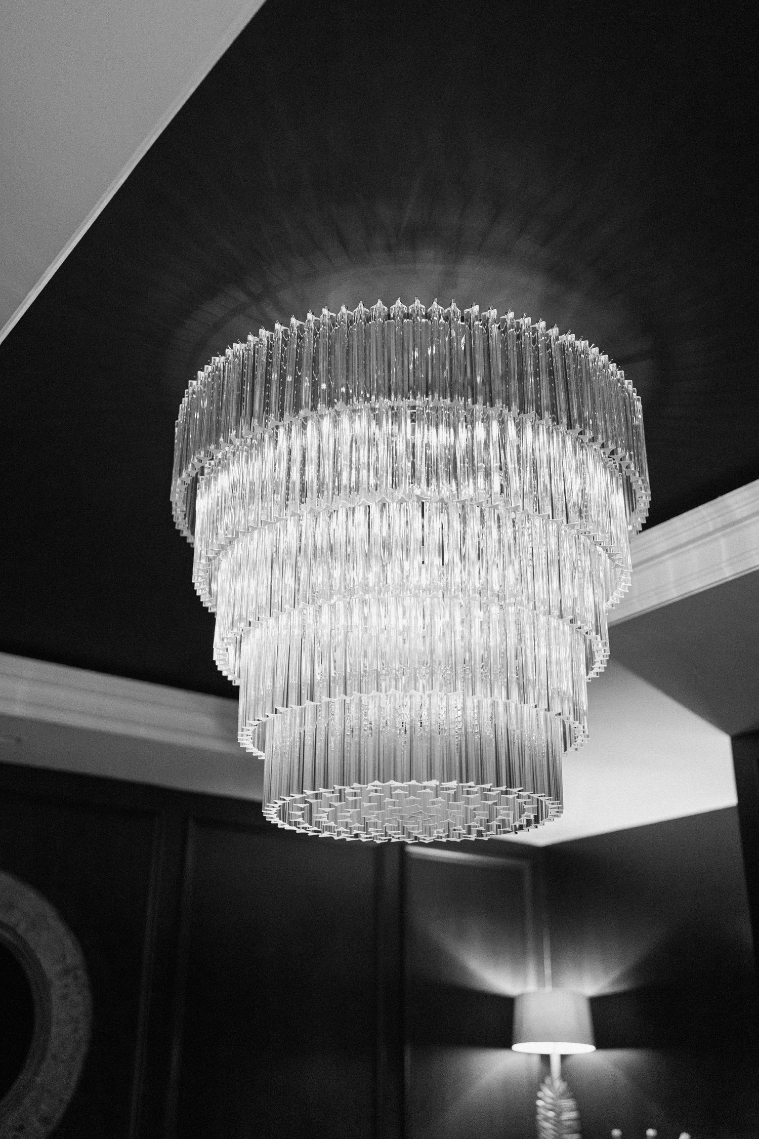 Elegant multi-tiered crystal chandelier photographed in black and white at wedding venue.