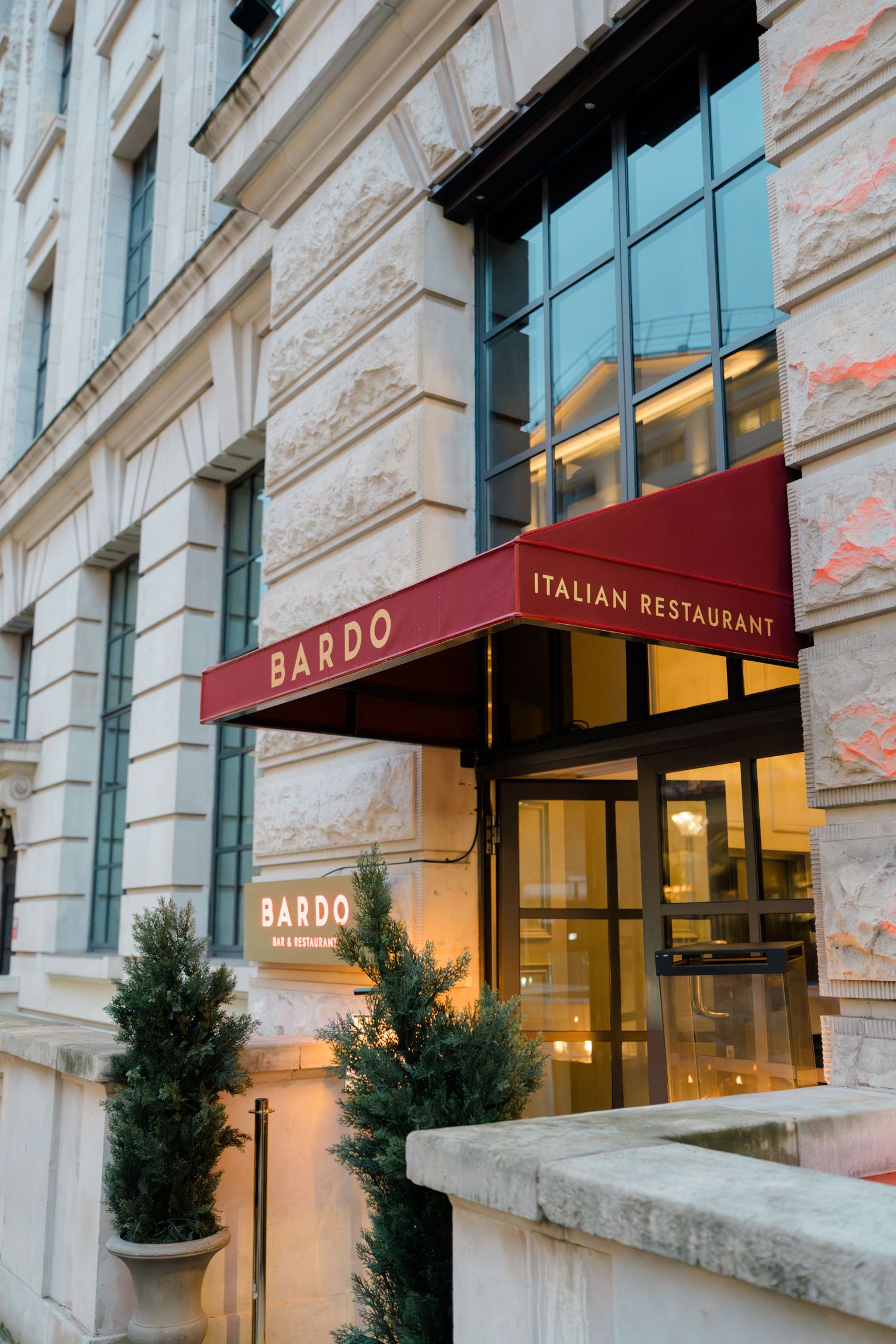 Exterior entrance of Bardo Italian Restaurant with a red awning at dusk.