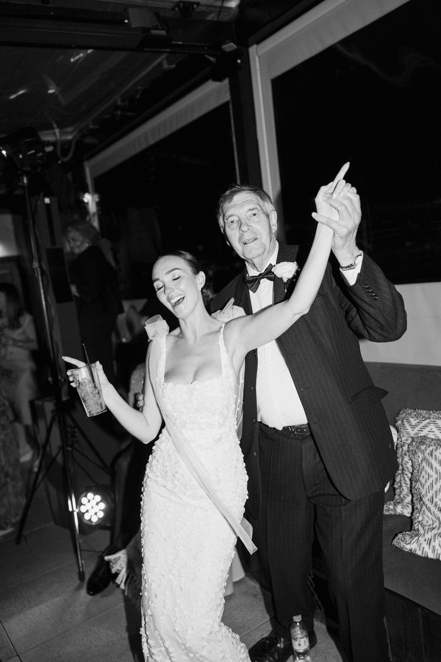 Bride and guests dancing with raised arms at wedding reception.