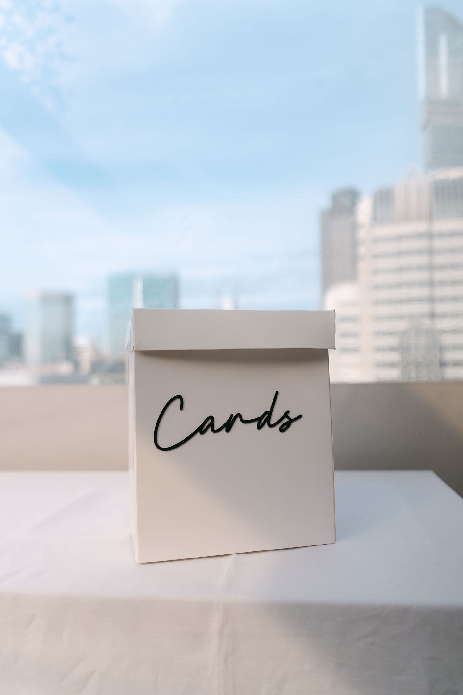 White wedding card box displayed on table with city skyline in background.