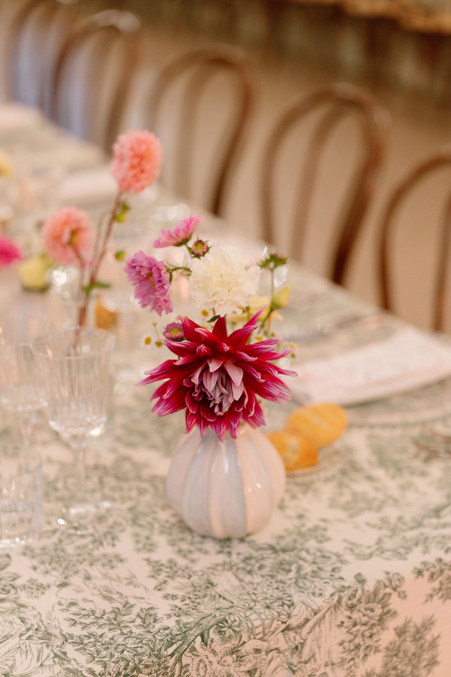 Delicate floral centerpieces with pink and burgundy blooms sit atop a patterned tablecloth at an elegant event.