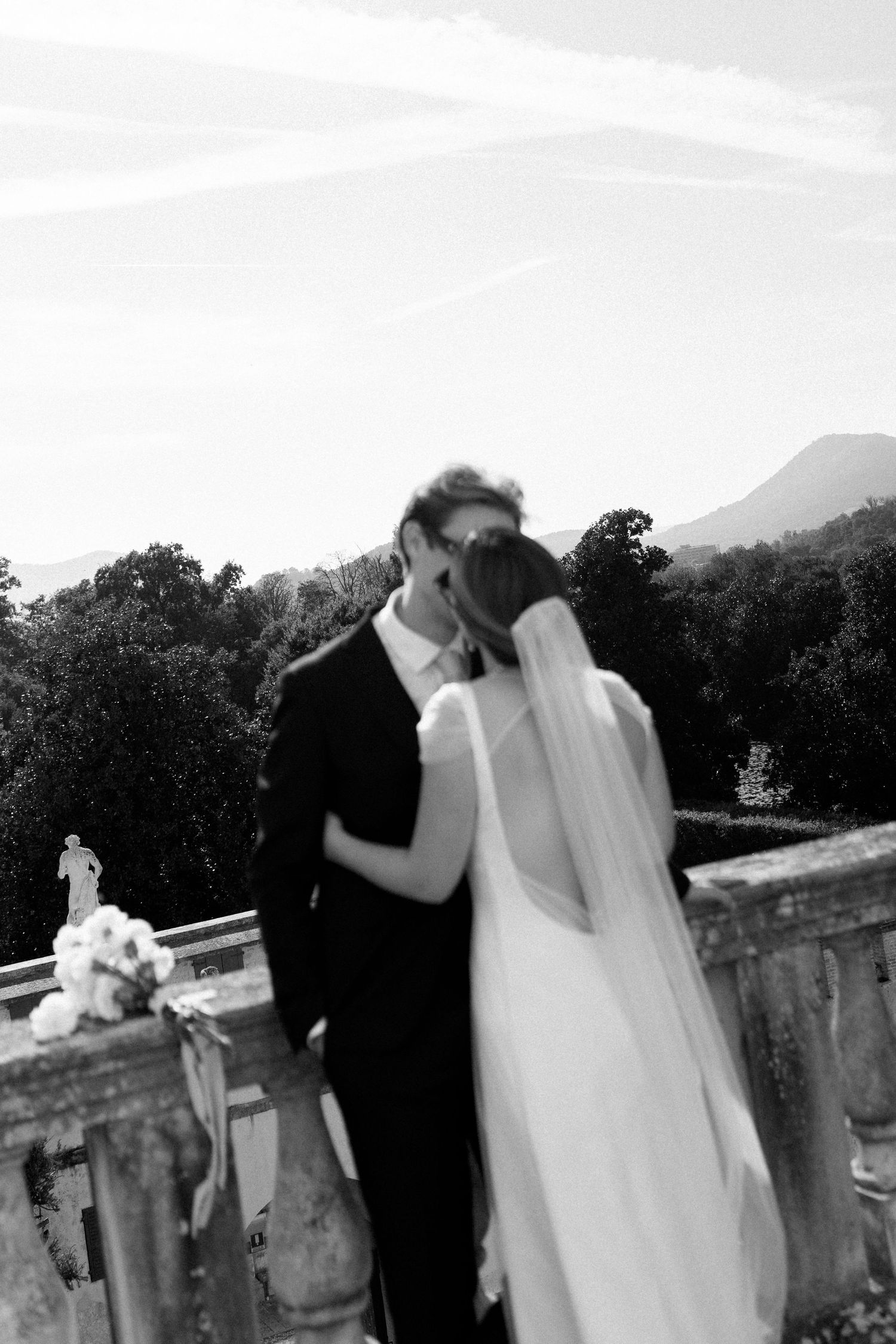 A tender moment between newlyweds on a stone balcony with mountains in the background.