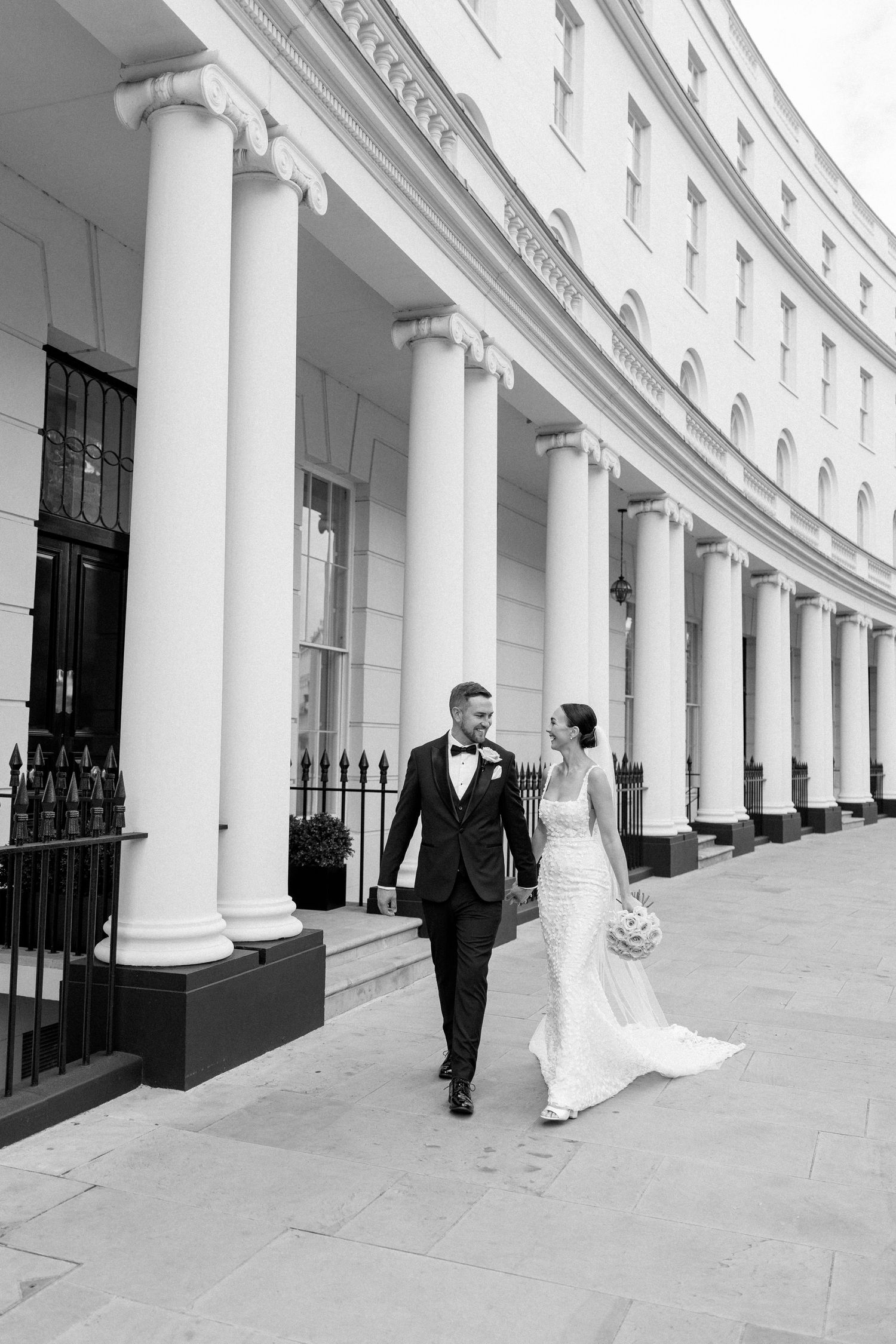 A happy couple walks along a classic Georgian building on their wedding day.