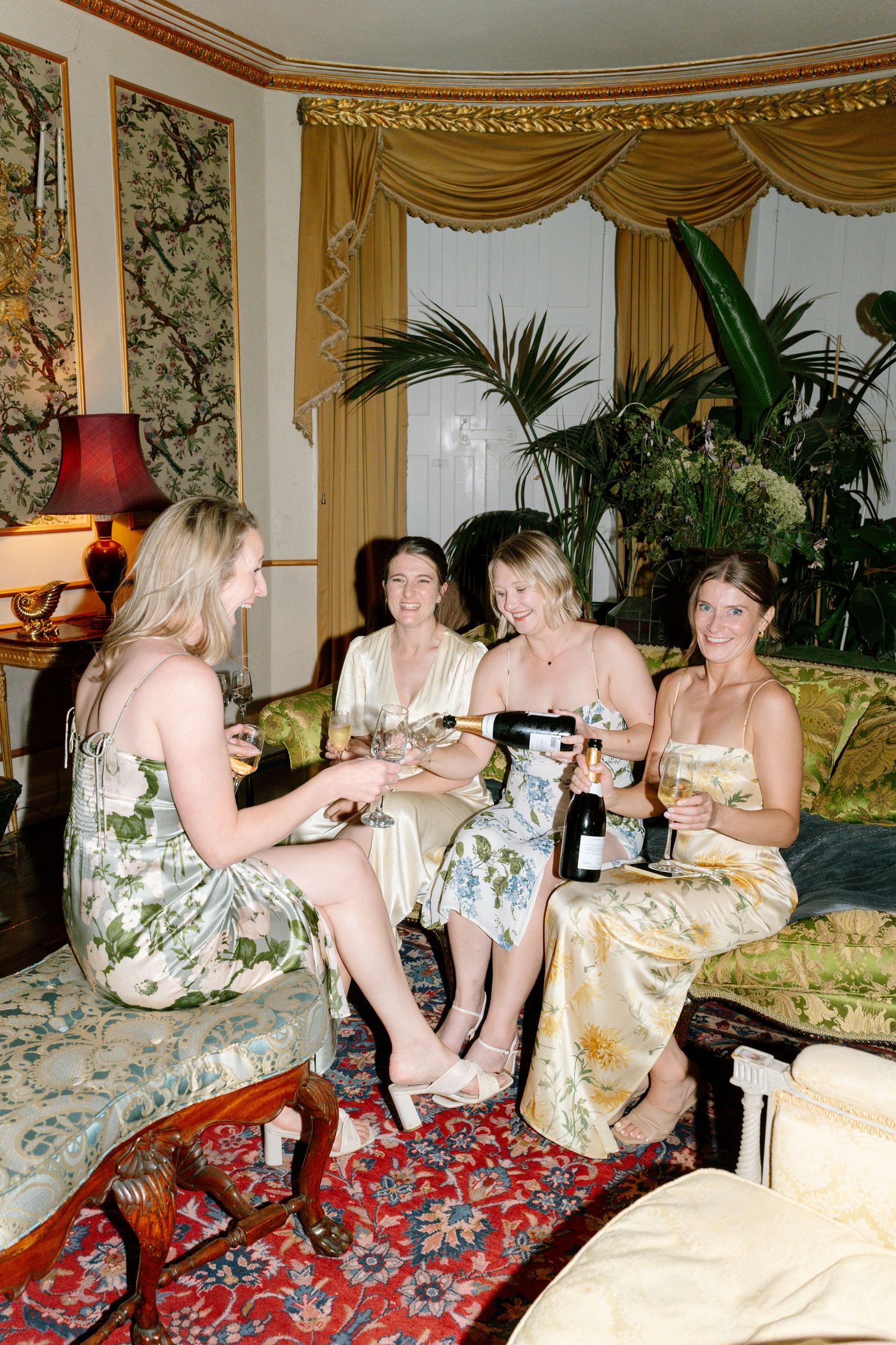 Group relaxing on ornate furniture in a luxurious room with palm plants and gold decor.