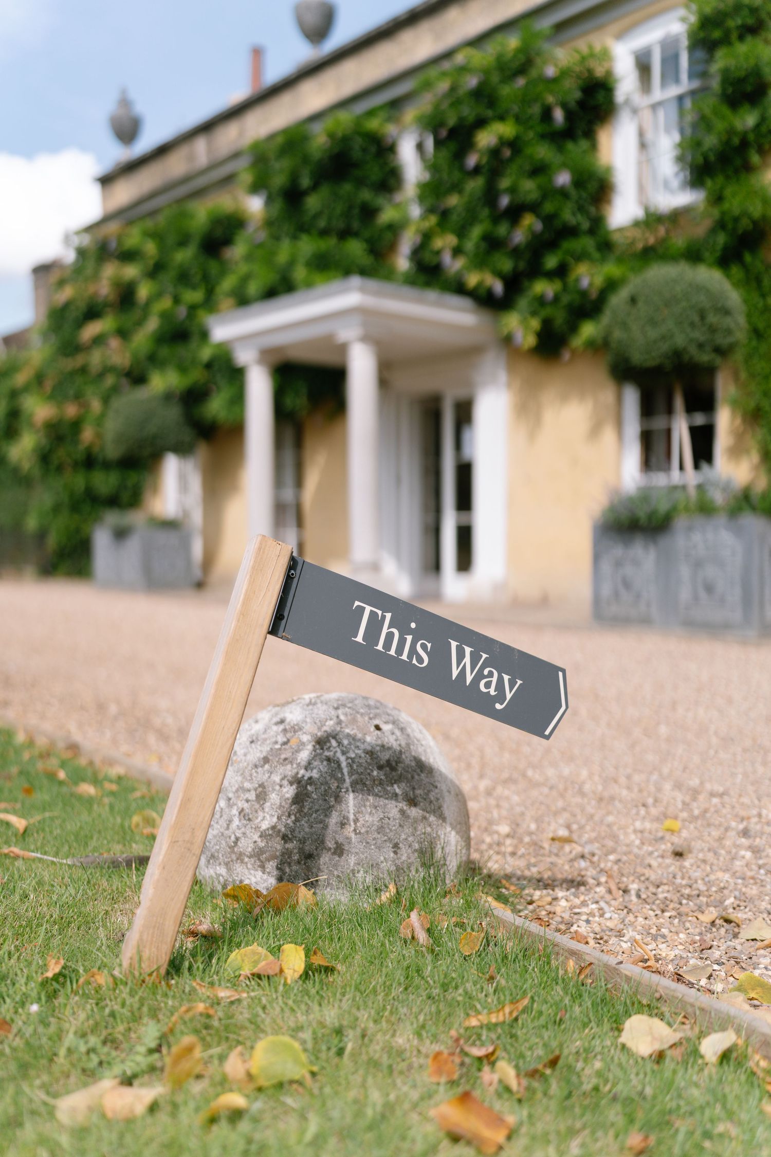 Directional sign reading 'This Way' in front of an ivy-covered country estate.