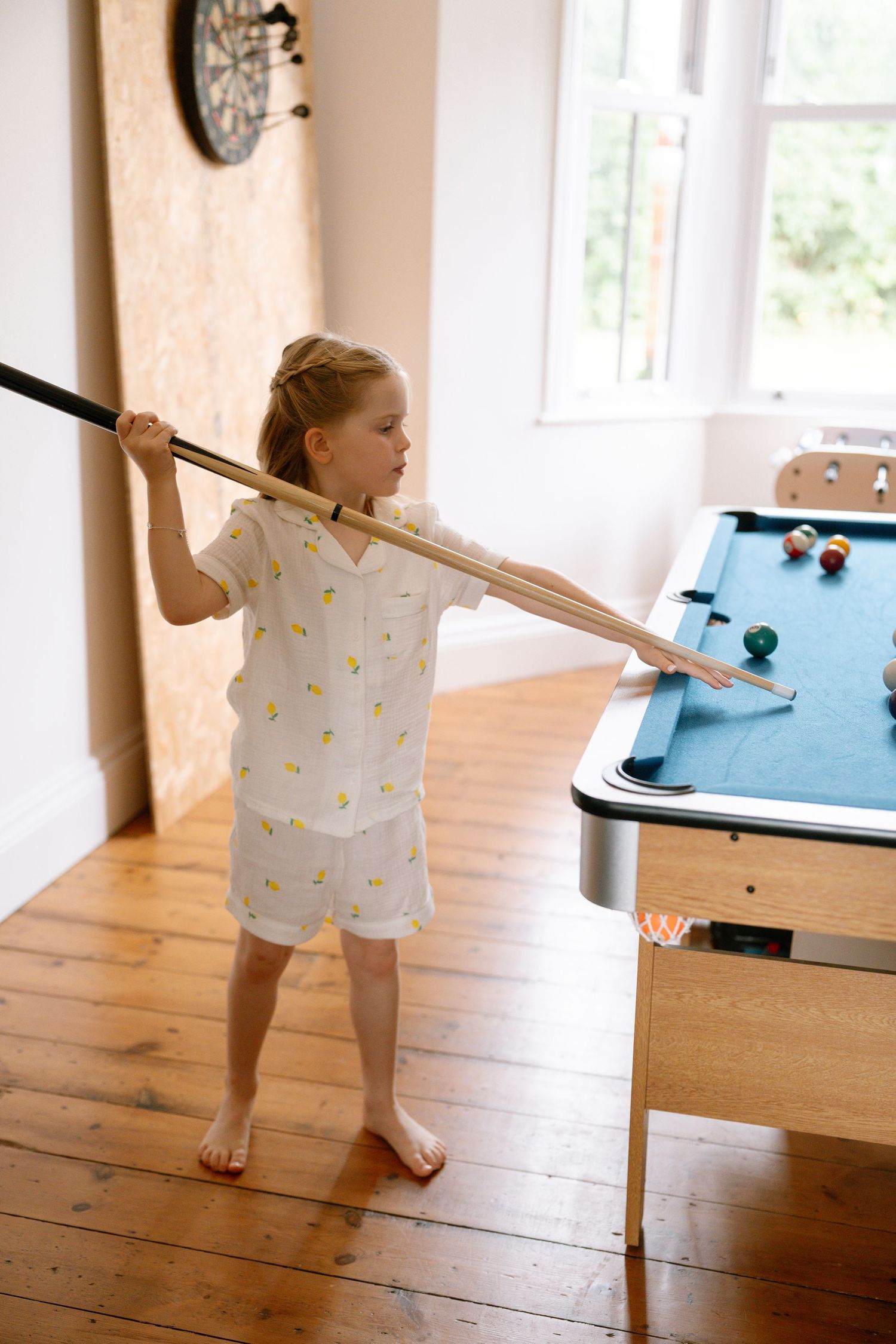 Young child in polka dot dress playing with pool cue beside blue pool table.