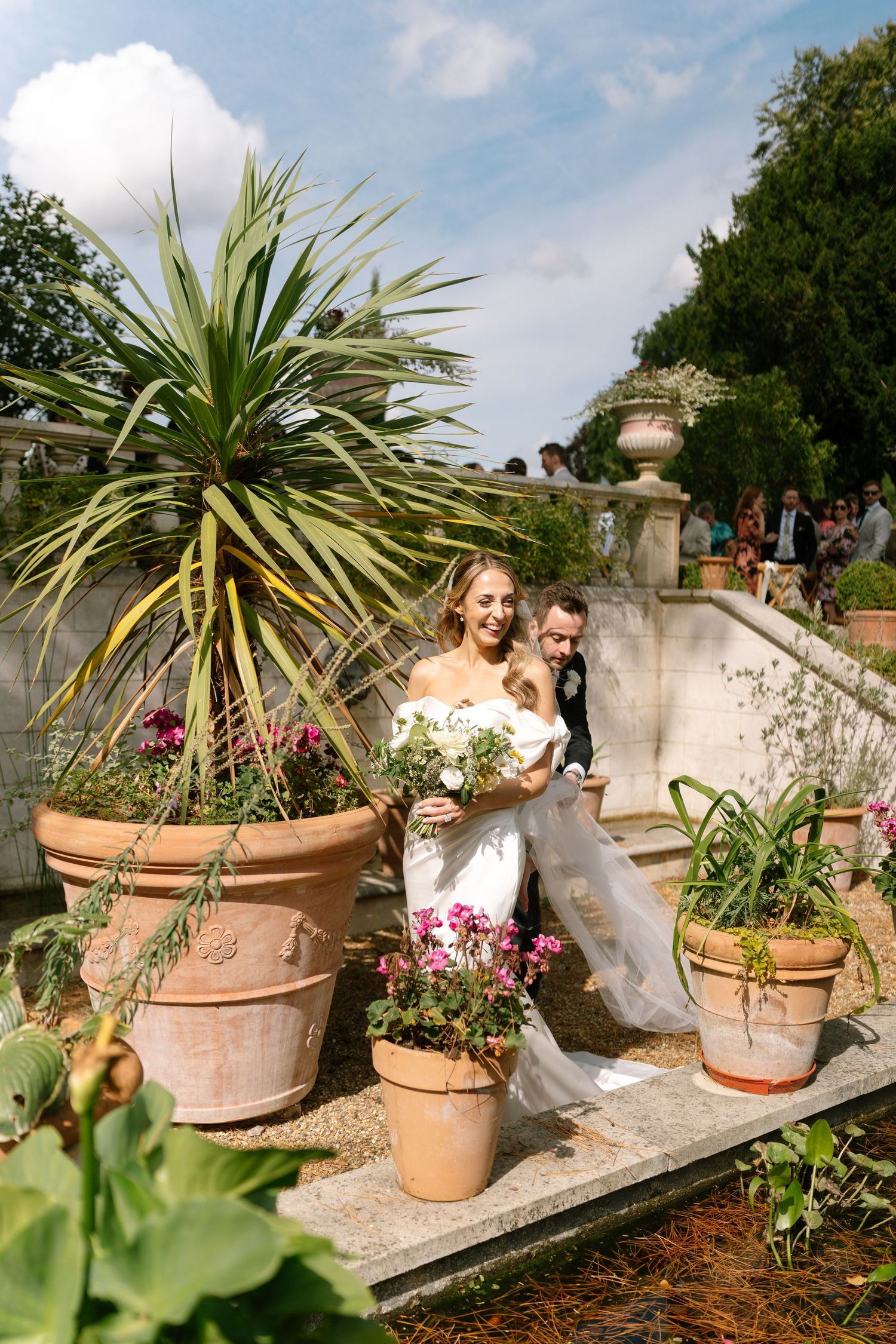Large terracotta planters with palm plants line stone steps in garden setting.