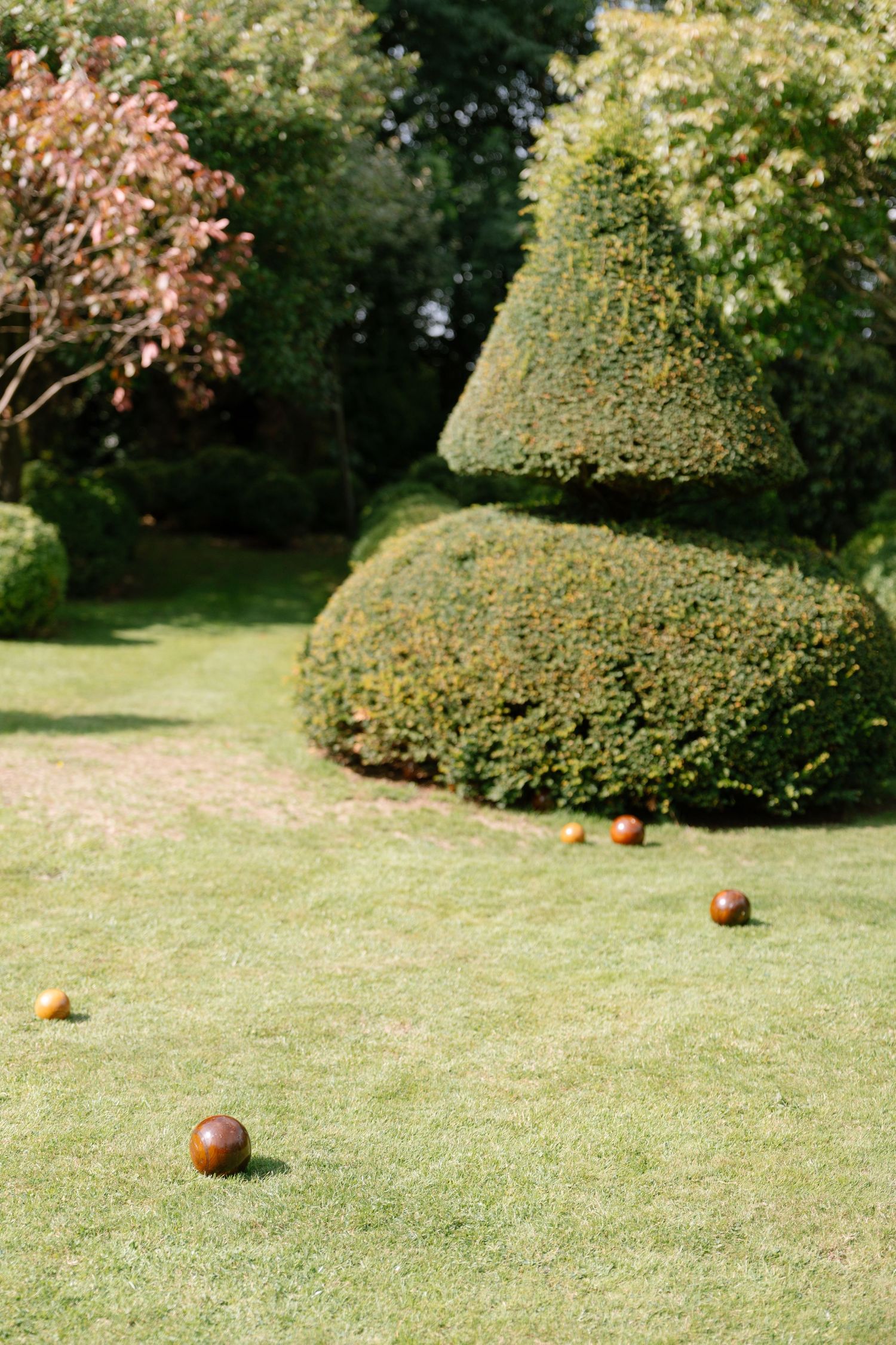 Sculpted topiary bushes and scattered apples on a manicured lawn create a whimsical garden scene.