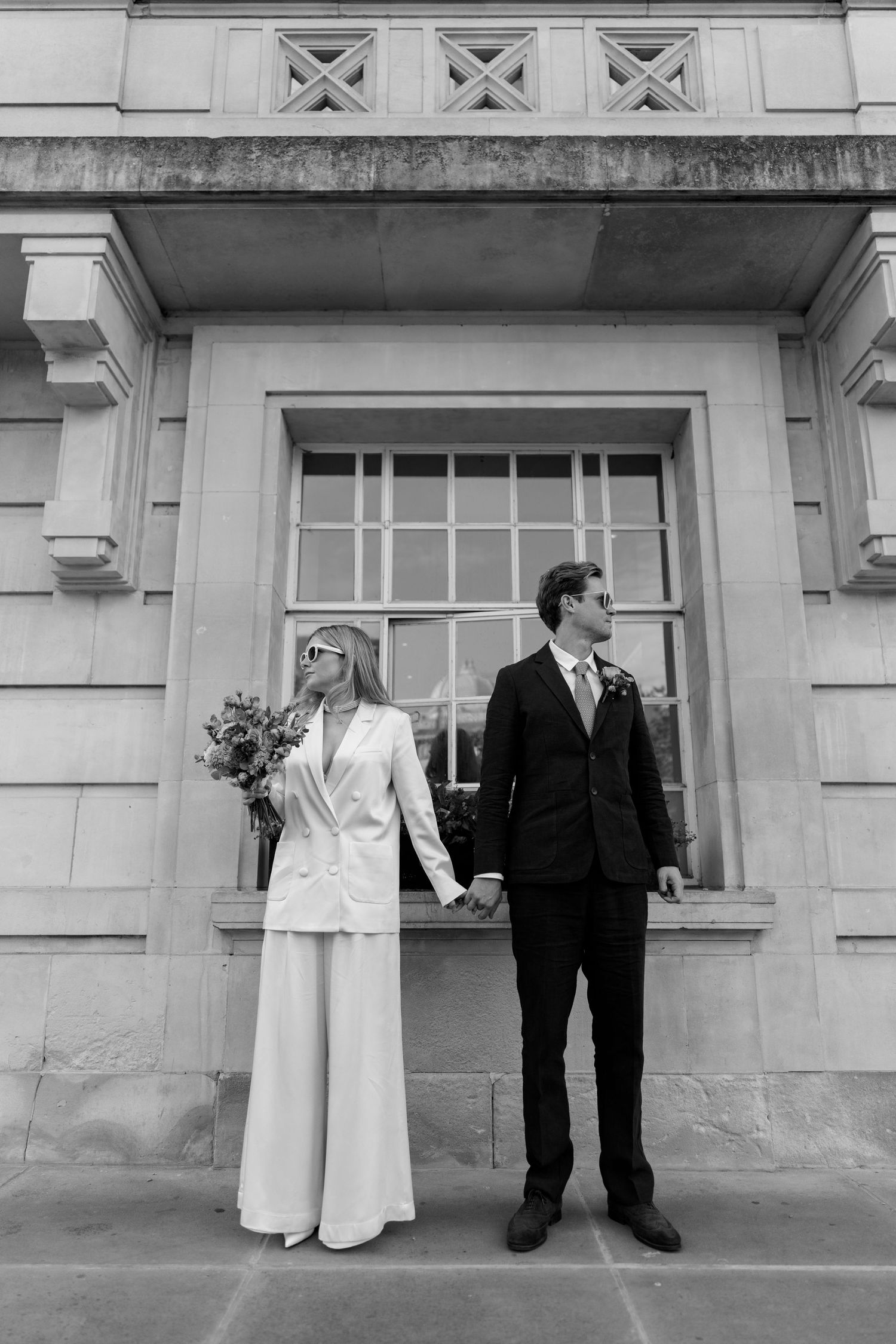 Black and white portrait of newlyweds standing by architectural window.