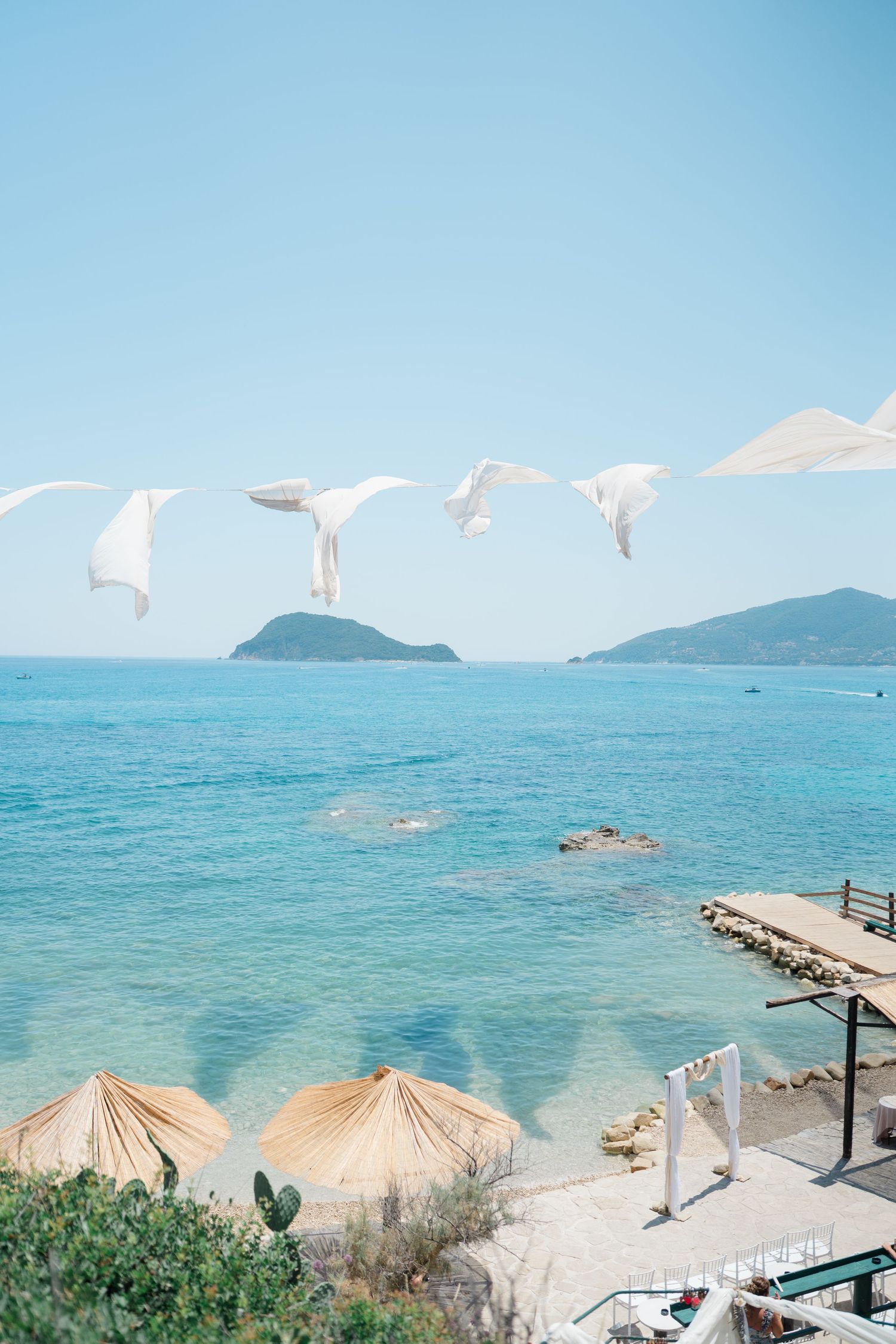 Beachfront view with thatched umbrellas and turquoise waters against mountainous backdrop.