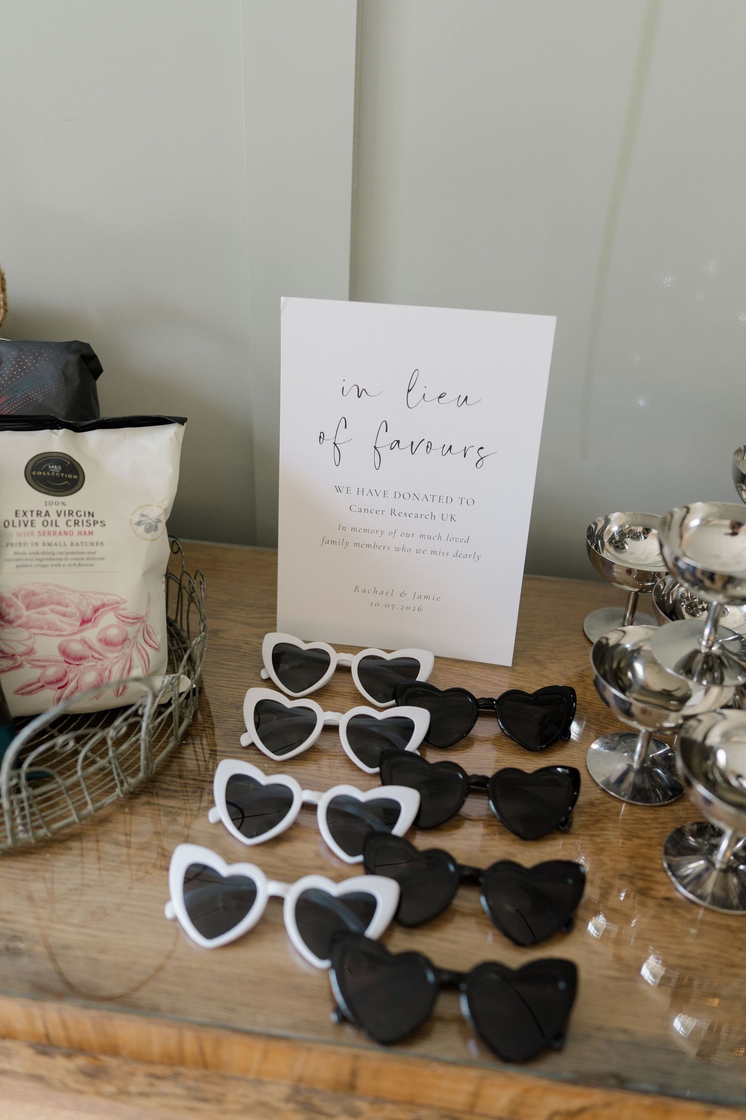 Heart-shaped sunglasses wedding favors displayed on table beside in lieu of favours charity donation sign.