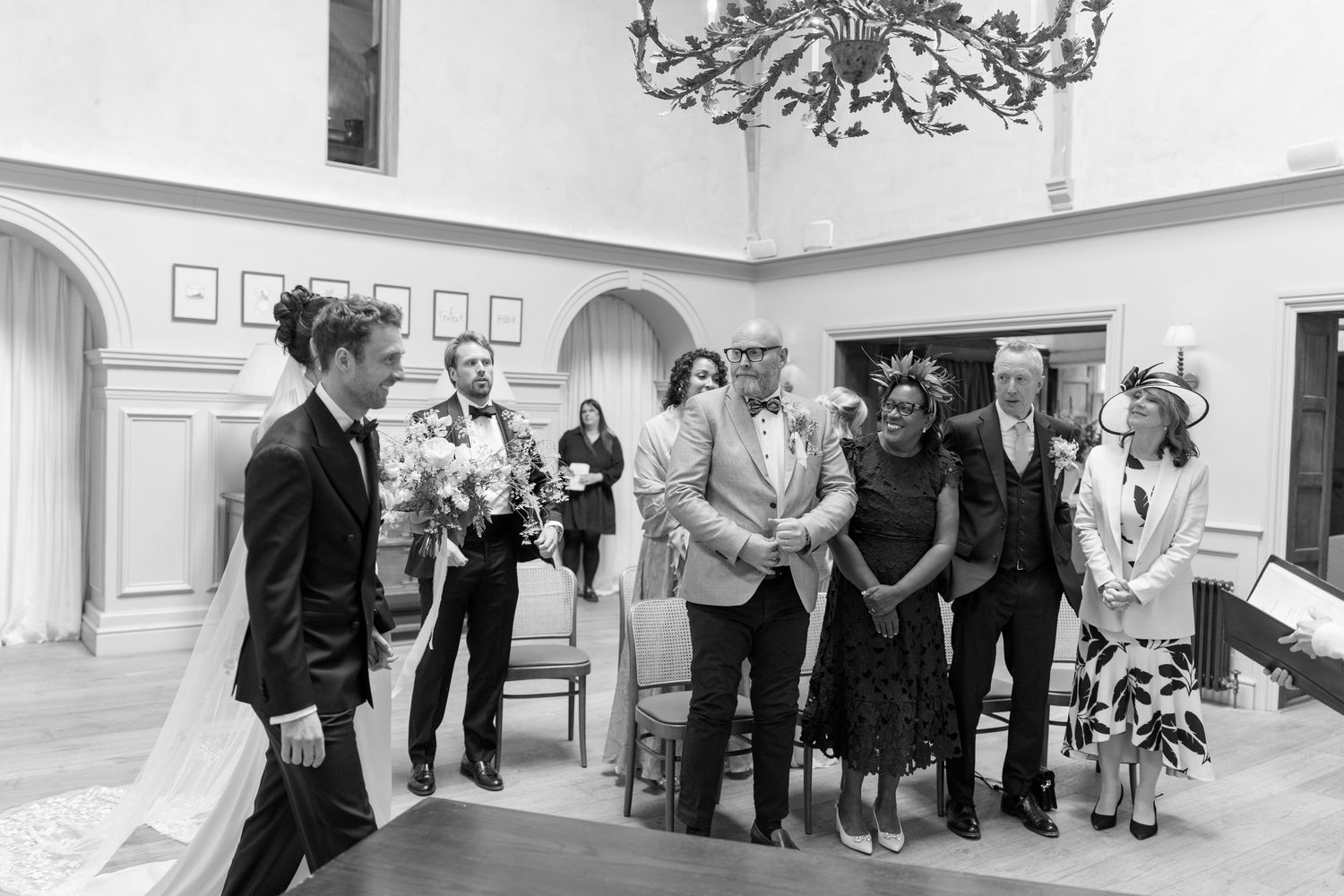 Wedding ceremony guests smiling and watching in a elegant room with chandelier in black and white.
