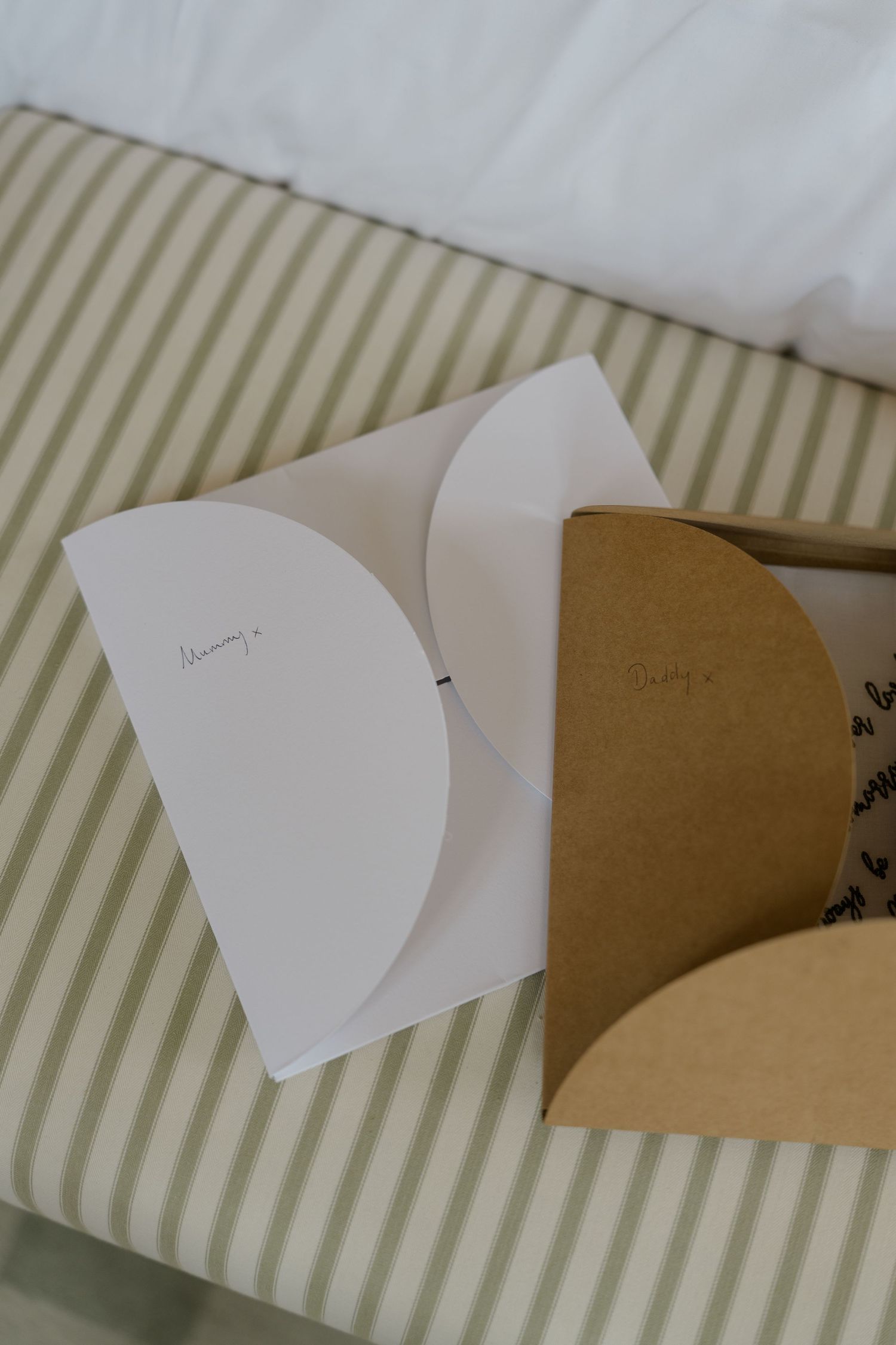 Two elegant wedding cards labeled Mummy and Daddy rest on a green striped bed.