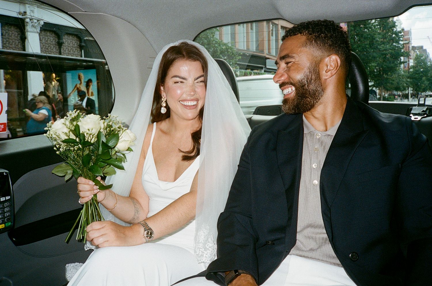 Happy bride and groom smiling together in a limousine, bride holding white flowers on their wedding day.