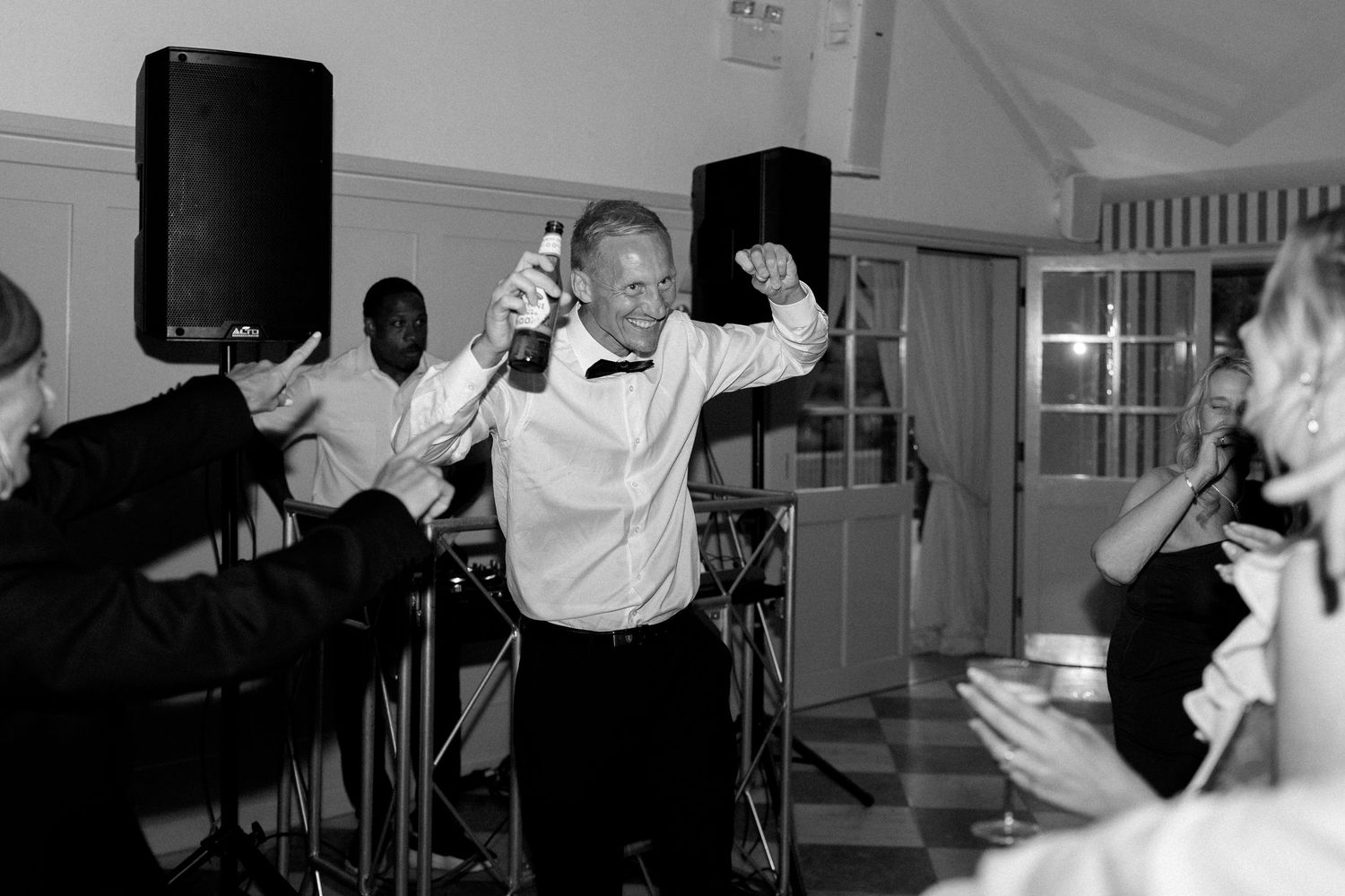 Energetic wedding guest dancing with champagne bottle raised at elegant black tie reception.