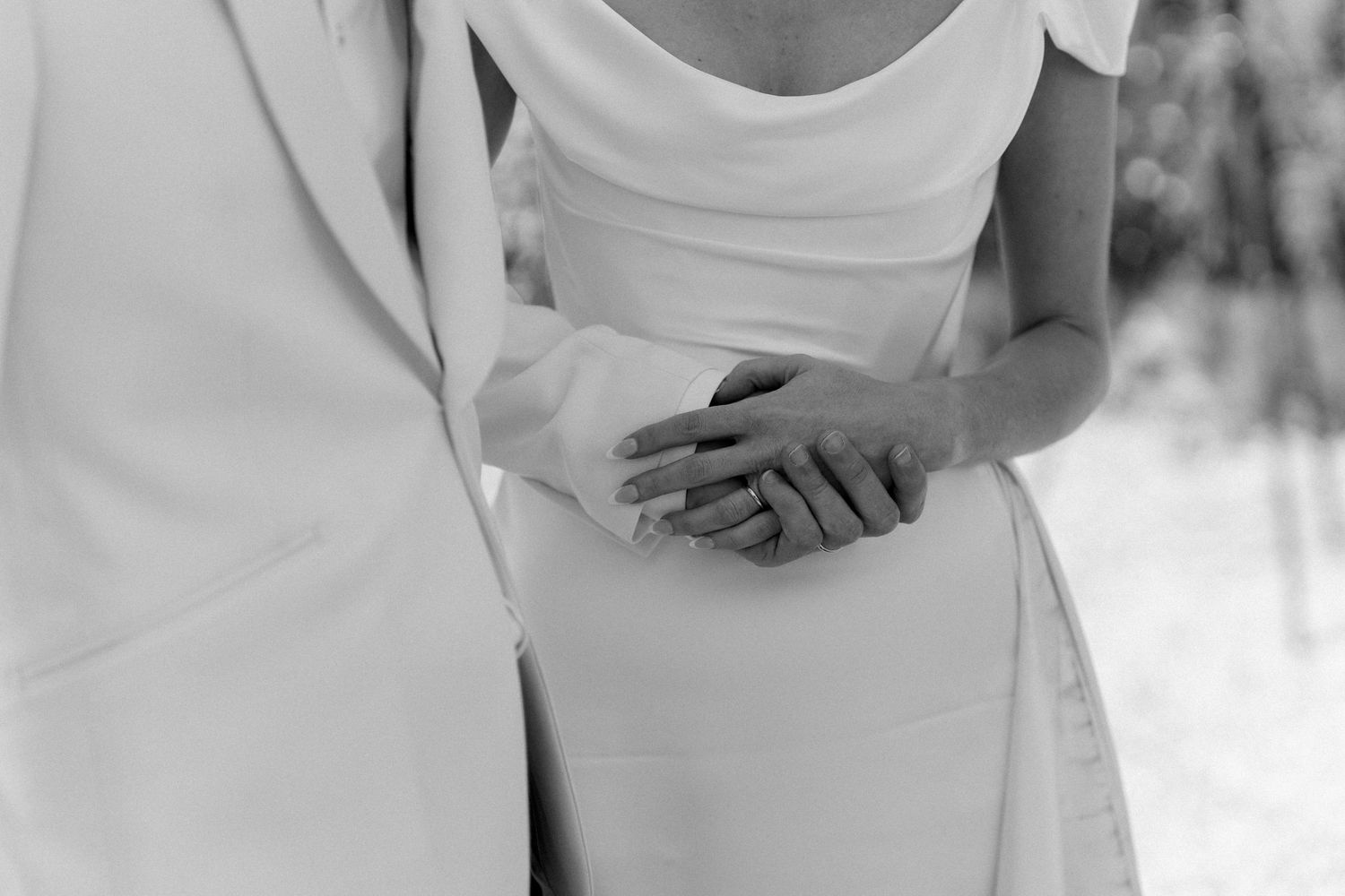 Black and white close-up of bride and groom holding hands in wedding attire.
