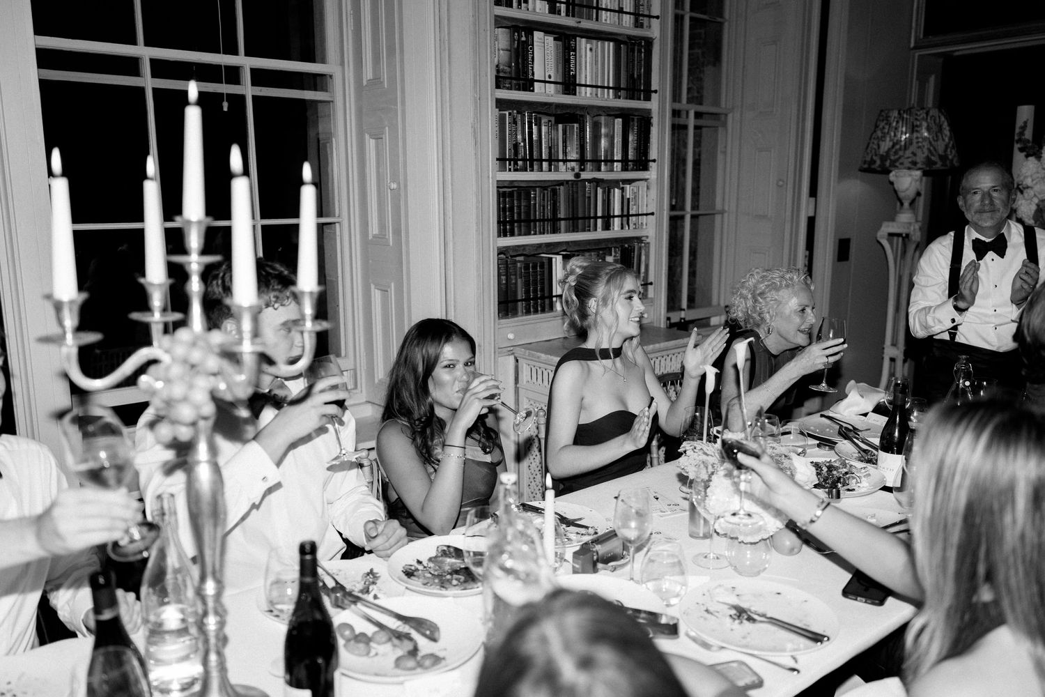 Black and white photo of guests dining by candlelight at wedding reception.