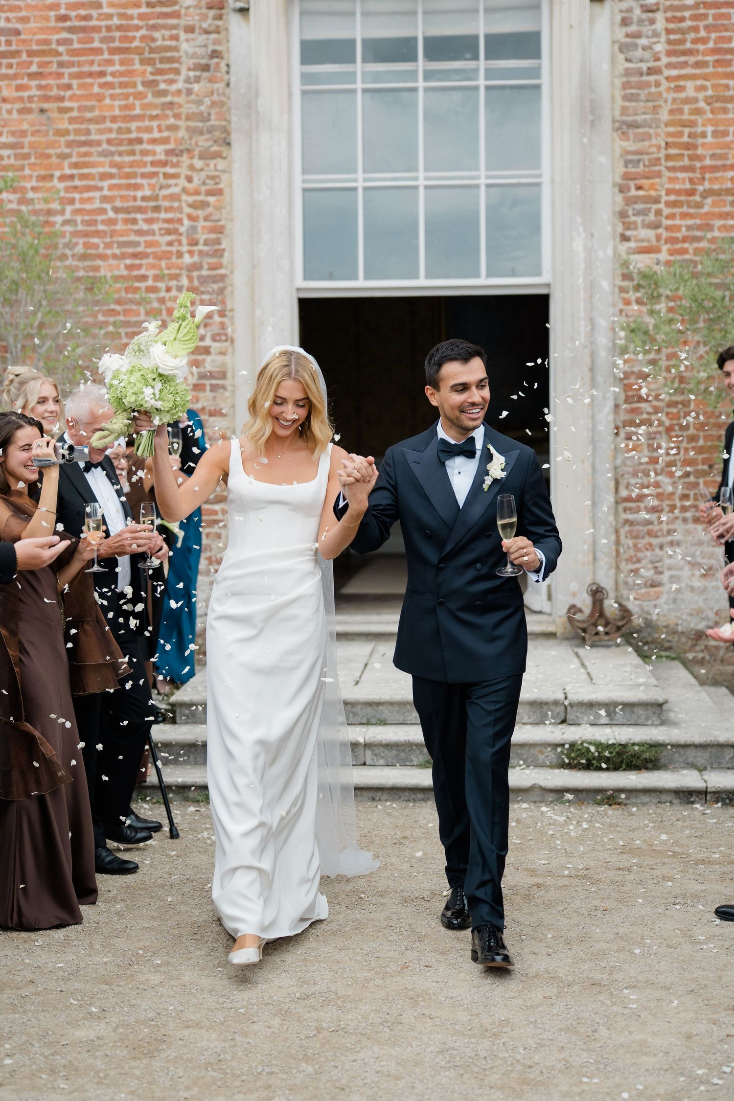 Newlyweds celebrating with confetti outside historic brick building after wedding ceremony.