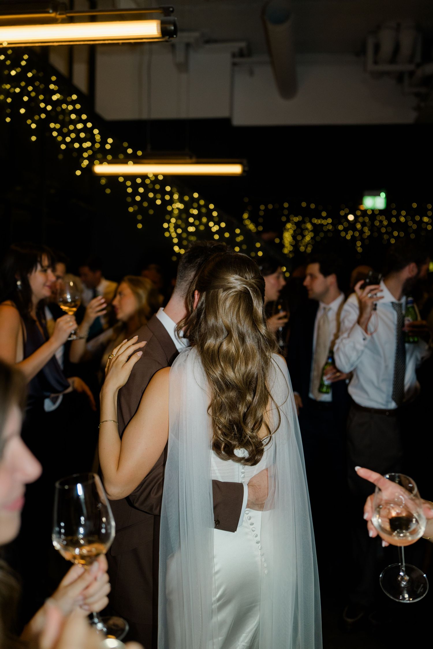 Bride in white satin gown with veil dancing with groom at evening wedding reception.