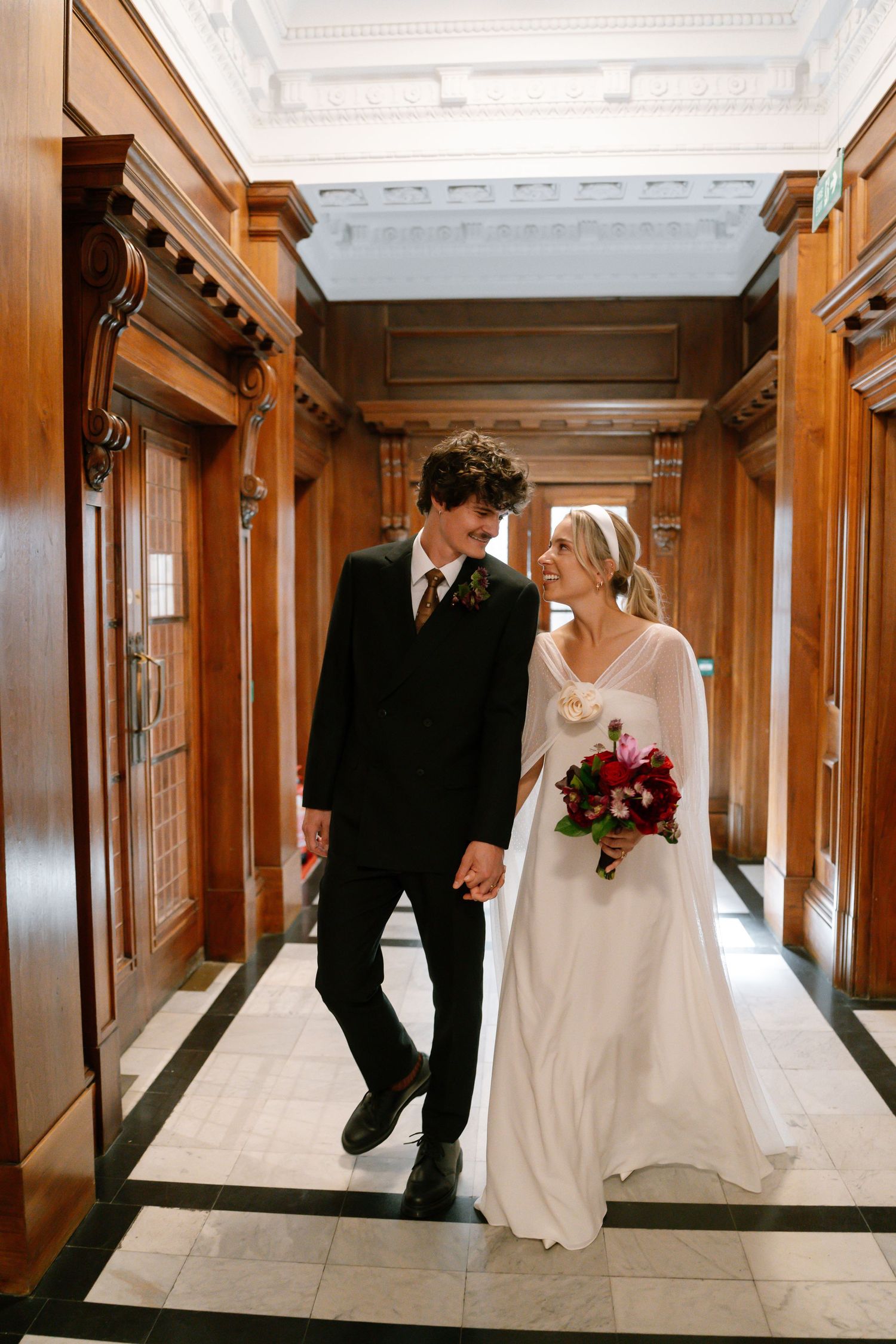 Couple walking through an elegant wood-paneled hallway during their wedding celebration.
