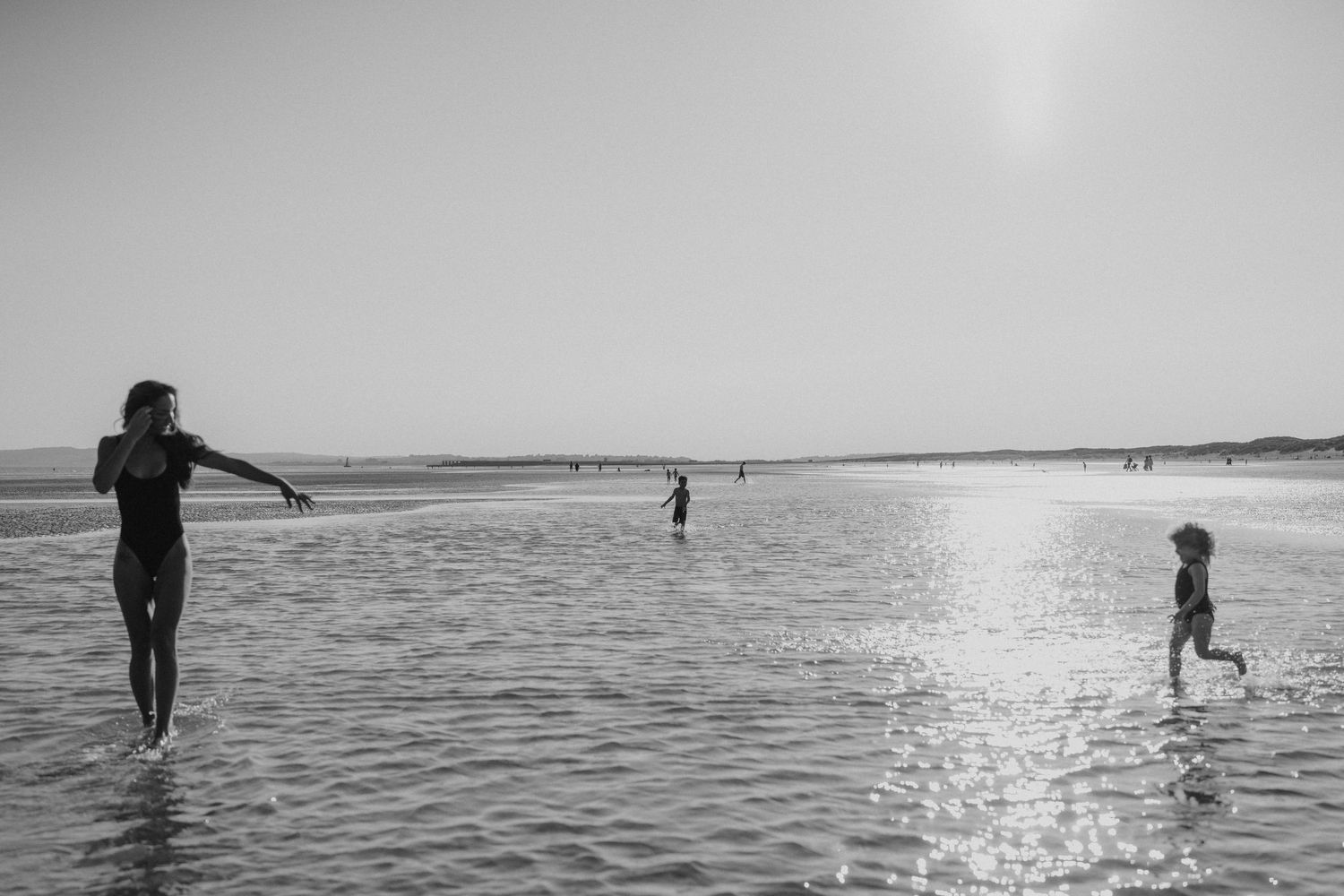 Silhouettes playing and splashing in shallow beach water at sunset.