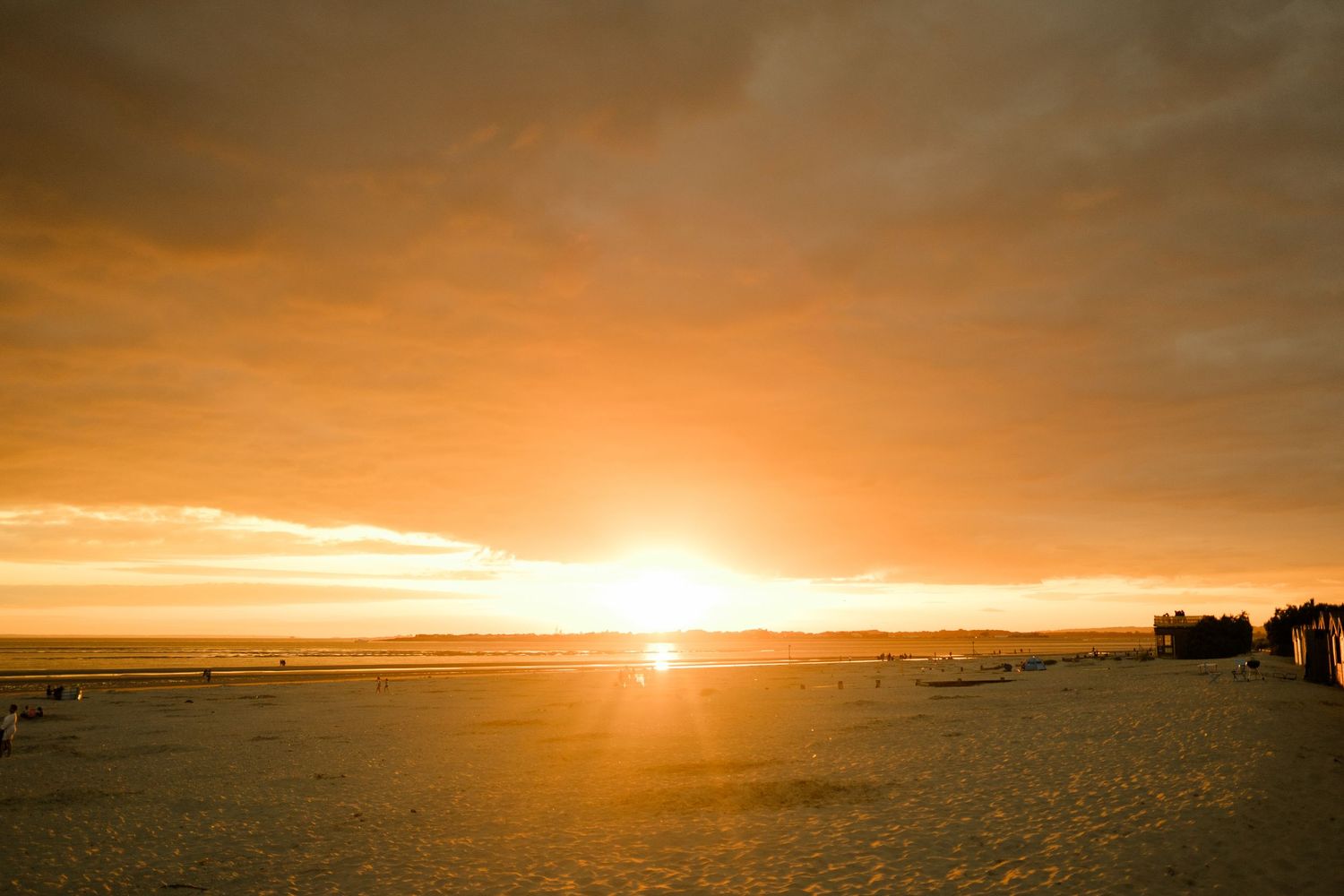 Dramatic orange sunset over a deserted beach with silhouettes of trees in the distance.