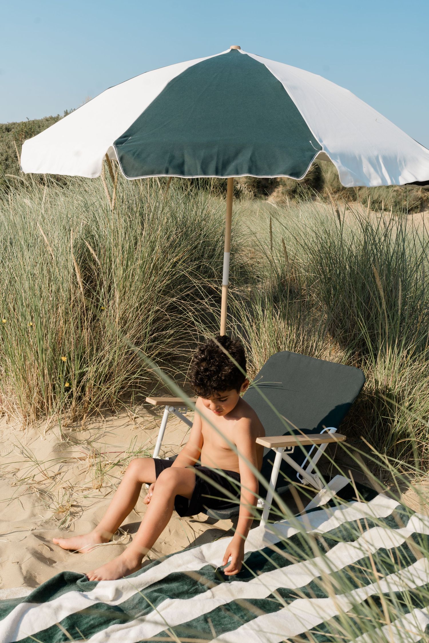 Beach scene with green umbrellas and striped blankets on sandy dunes.