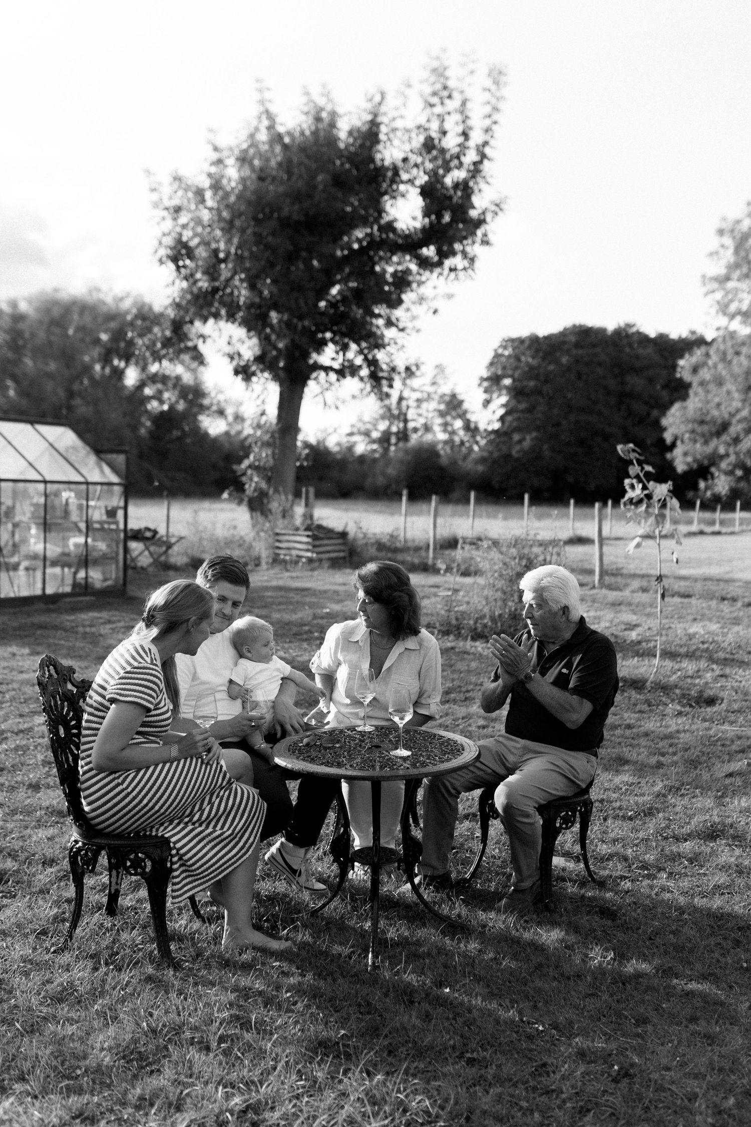 Group gathered around outdoor table for casual meal in black and white photography.