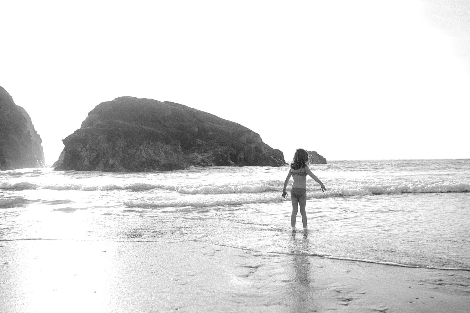 Silhouetted figures walking along misty beach with dramatic coastal rock formations.