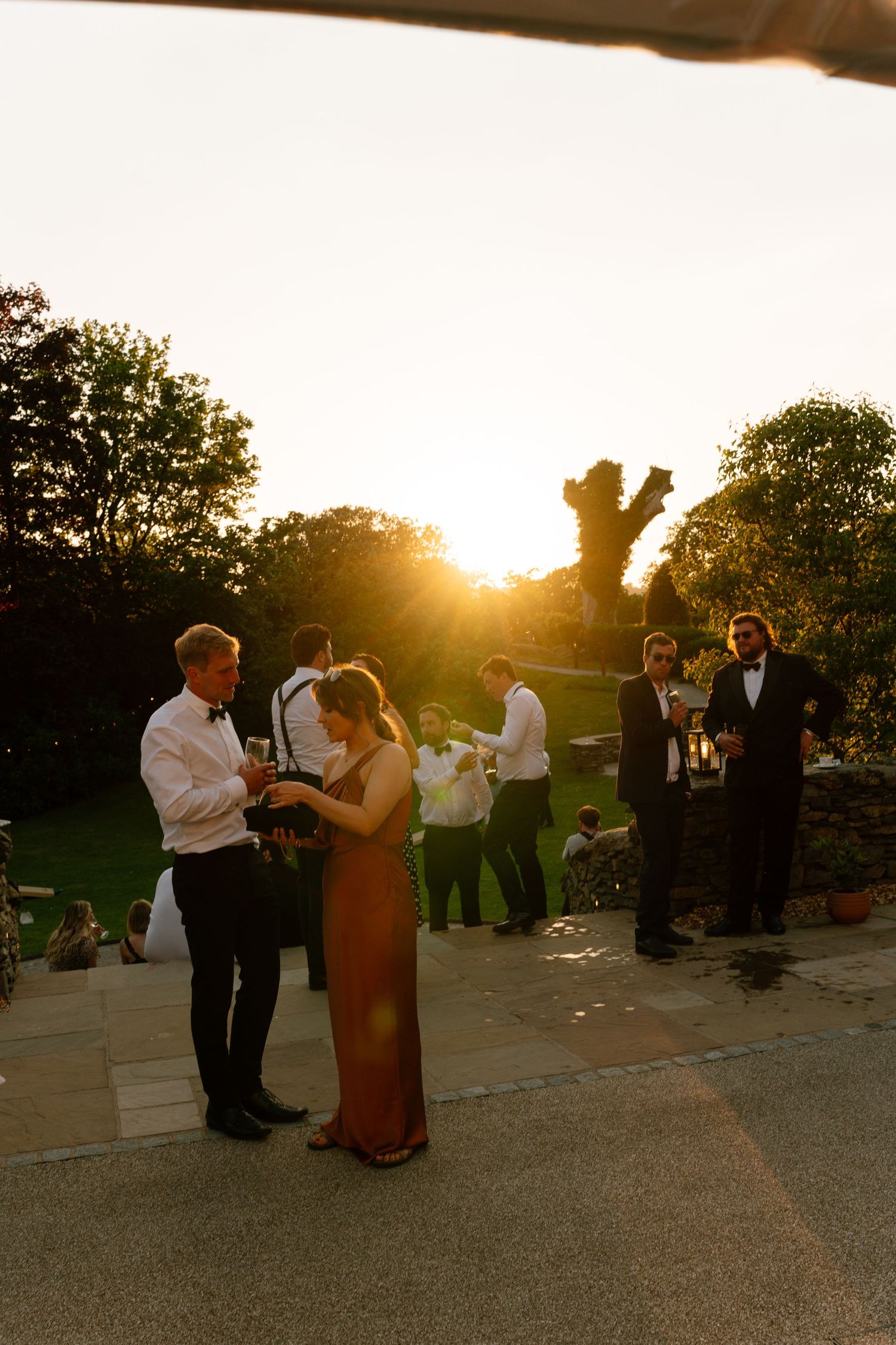 Wedding guests dance at sunset during outdoor reception celebration.