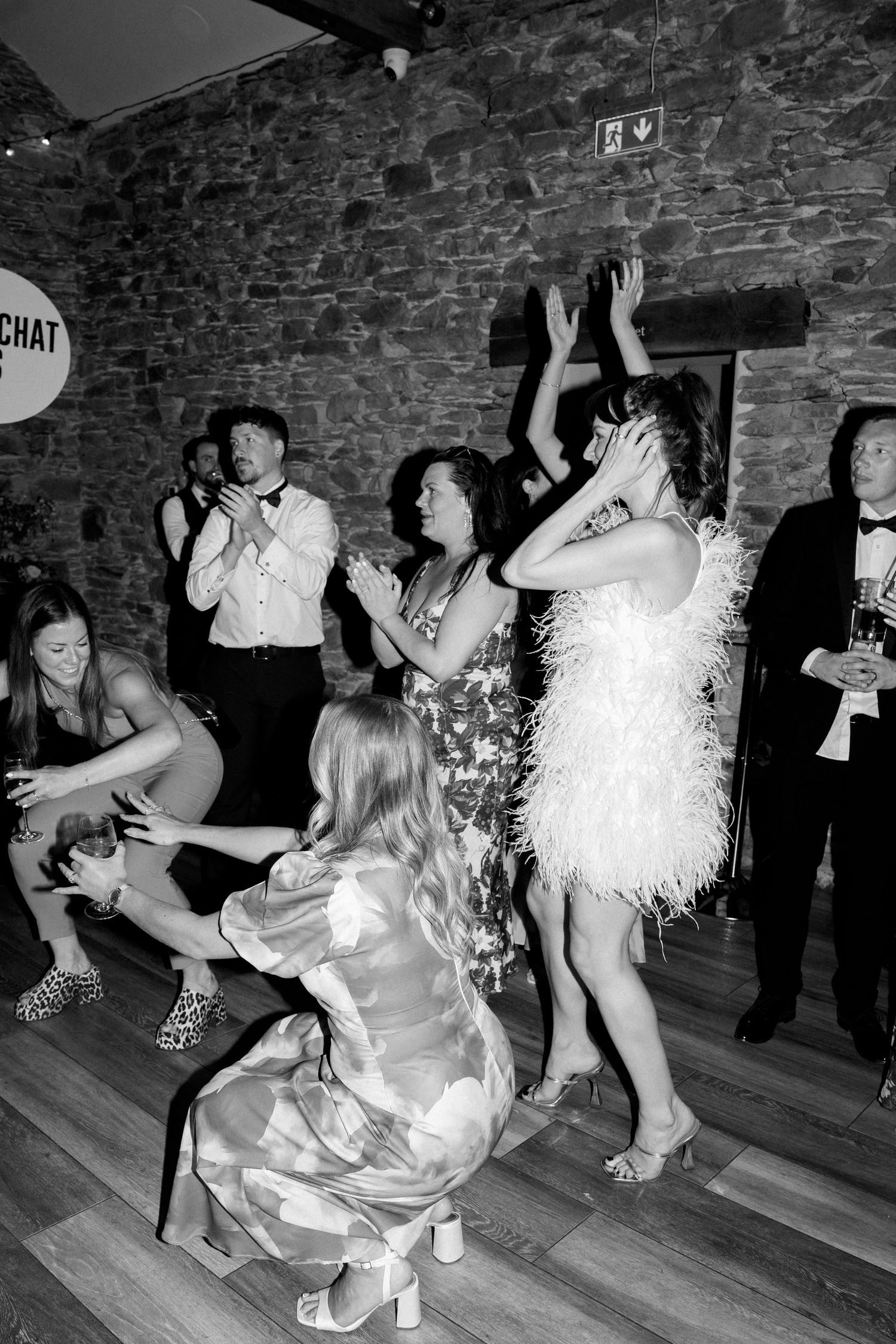 People dancing and celebrating at a party in a dimly lit stone interior venue.