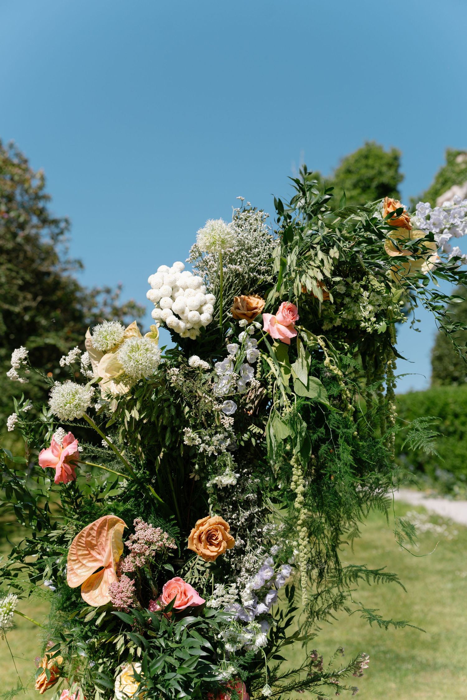 Elegant floral arrangement with pink and peach roses mixed with white flowers against a blue sky backdrop.