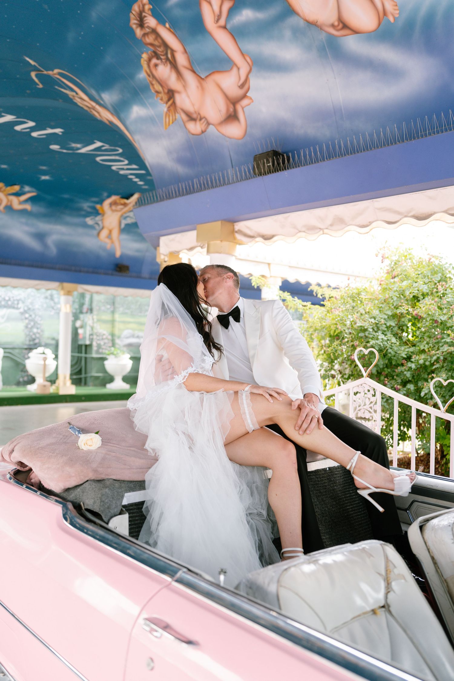 Couple poses in vintage pink car with flowing white dress.