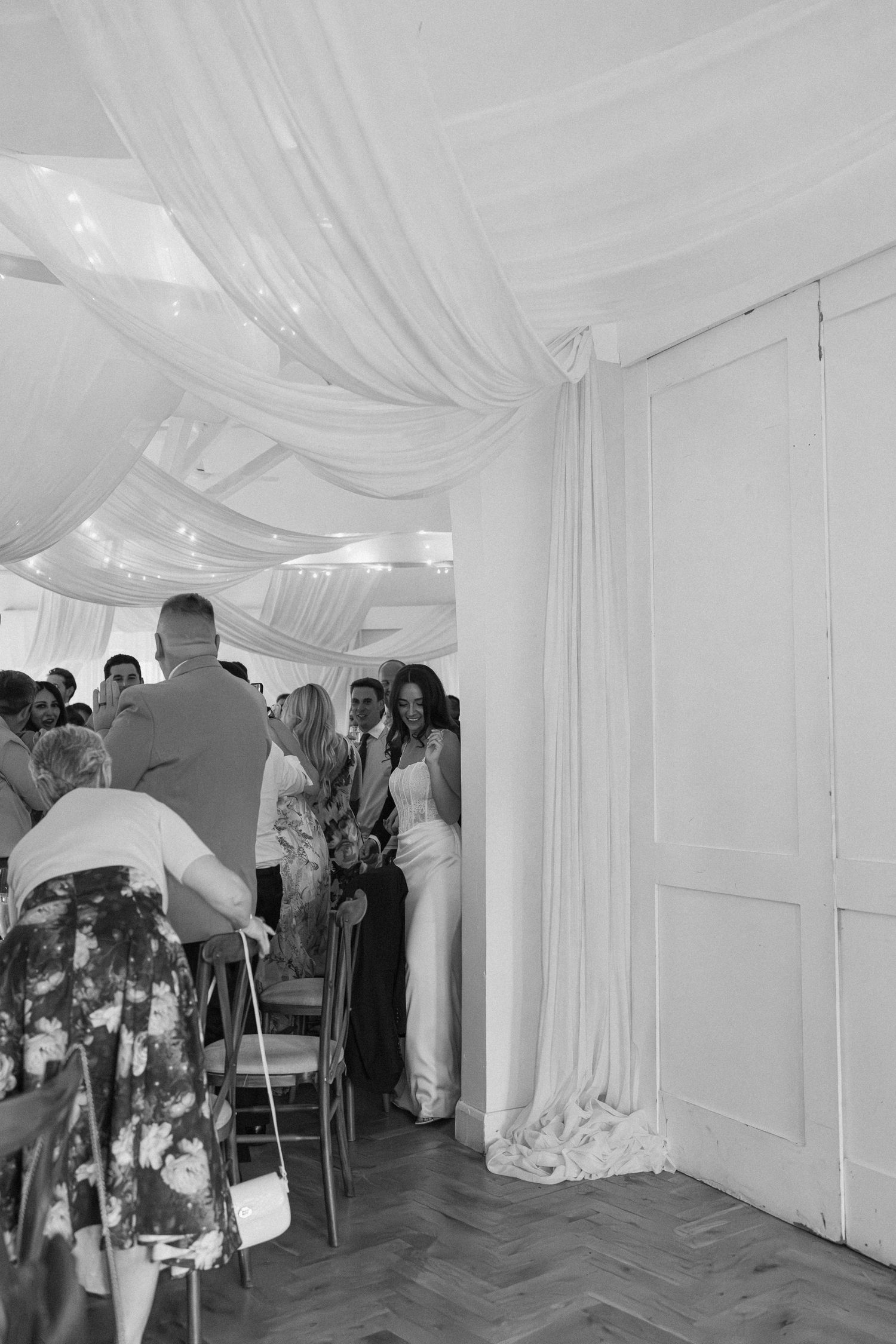 Bride enters draped wedding ceremony room as seated guests turn to watch her elegant entrance.